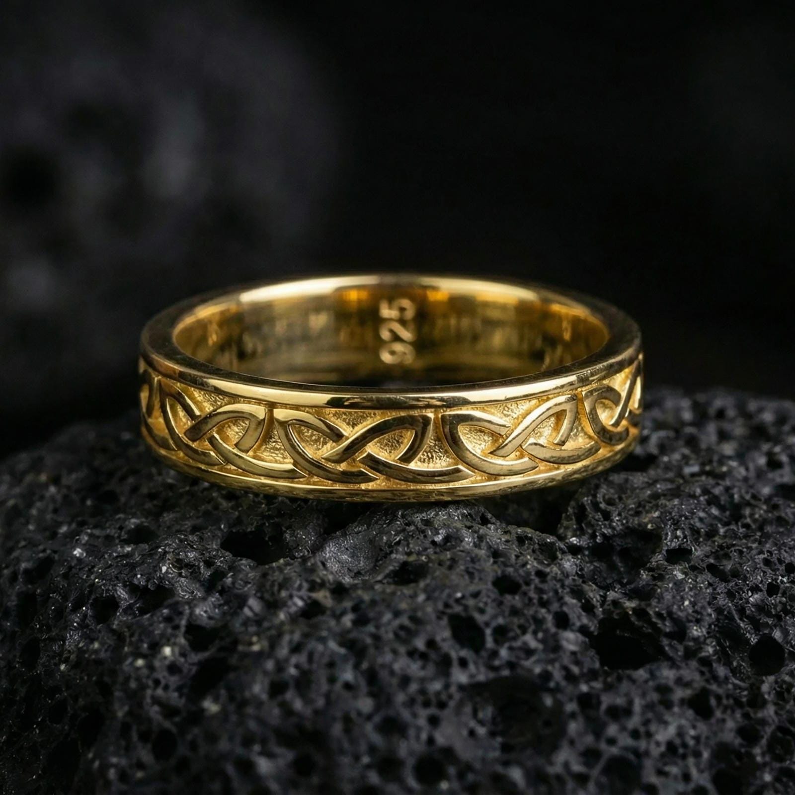 Gold plated Celtic knot band ring on volcanic stone, premium close-up highlighting warm gold tone across the woven pattern and smooth rounded profile.