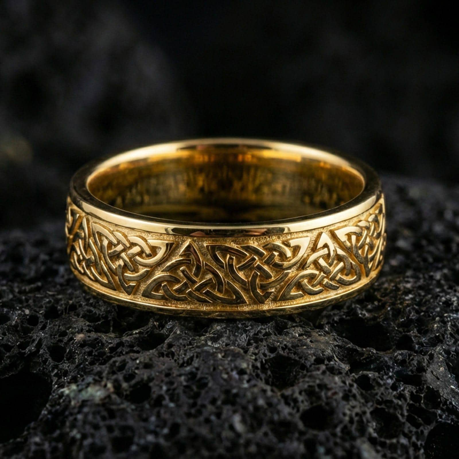Gold plated Celtic knot band ring on volcanic stone, premium macro shot showing warm gold tone across the woven knot pattern and smooth rounded profile.