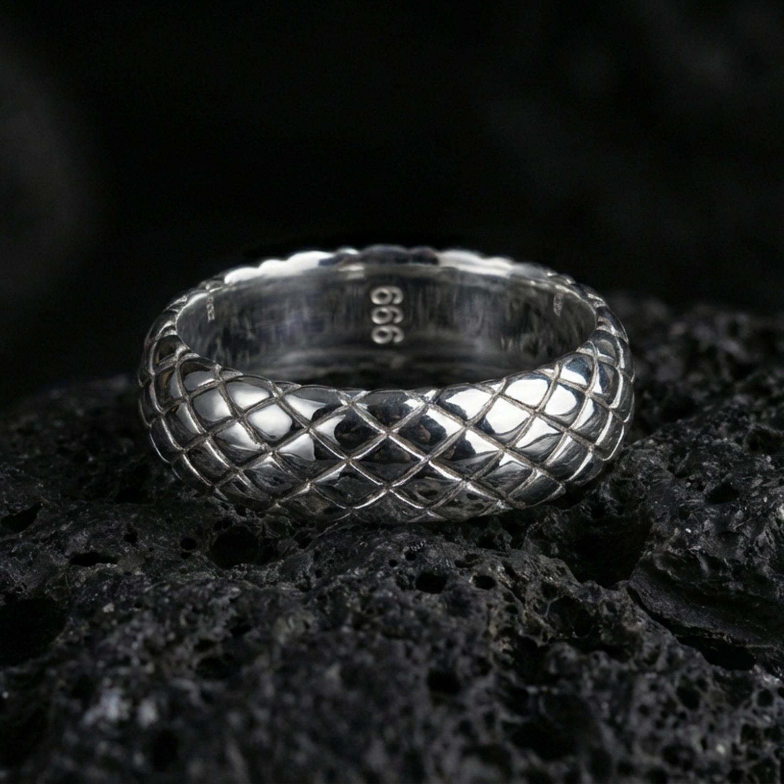 Polished silver woven texture band ring on volcanic stone, sharp macro product photo emphasizing clean reflections and crisp crosshatch detail.