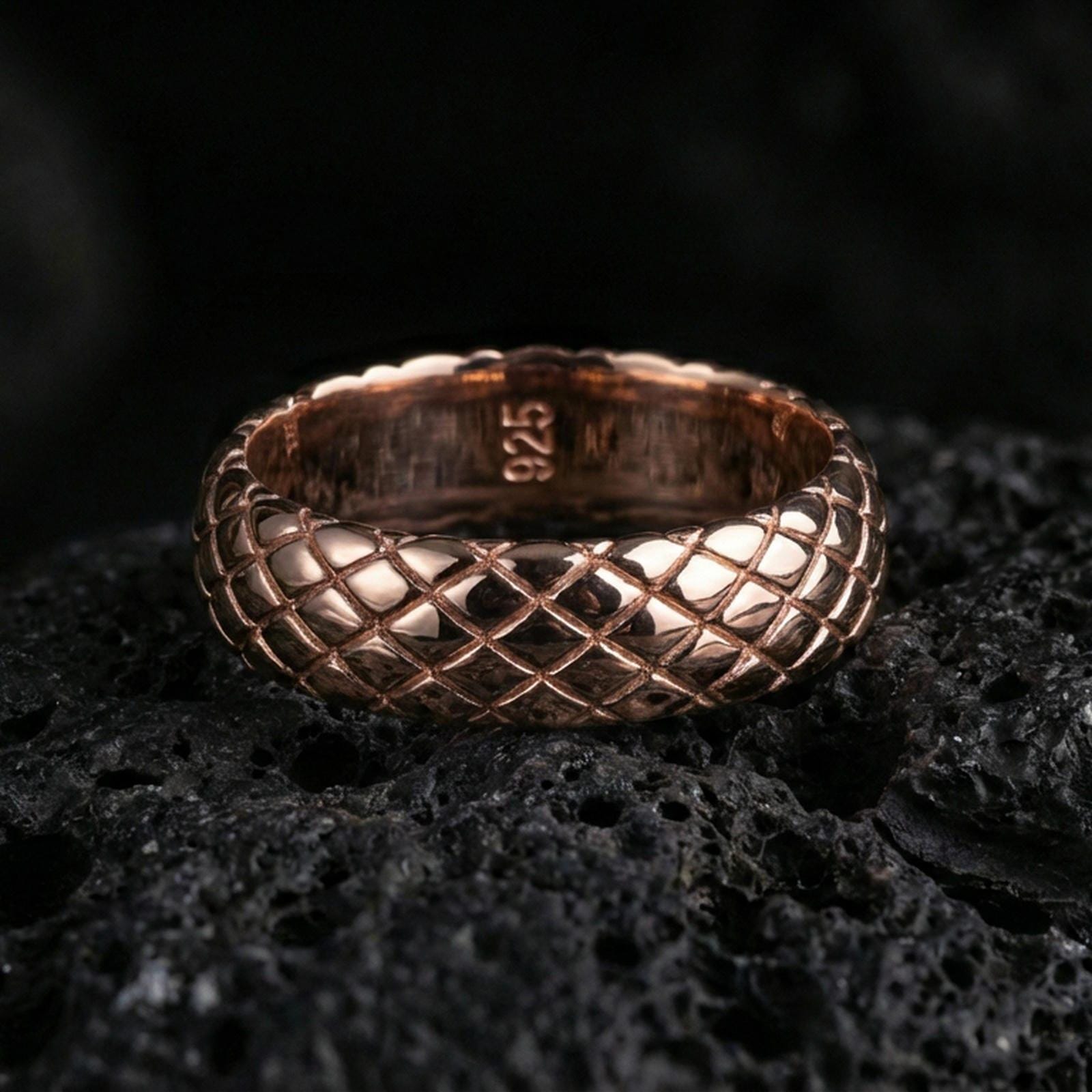 Rose gold plated woven texture band ring on volcanic stone, refined macro shot with soft rosy highlights and clear woven texture definition.