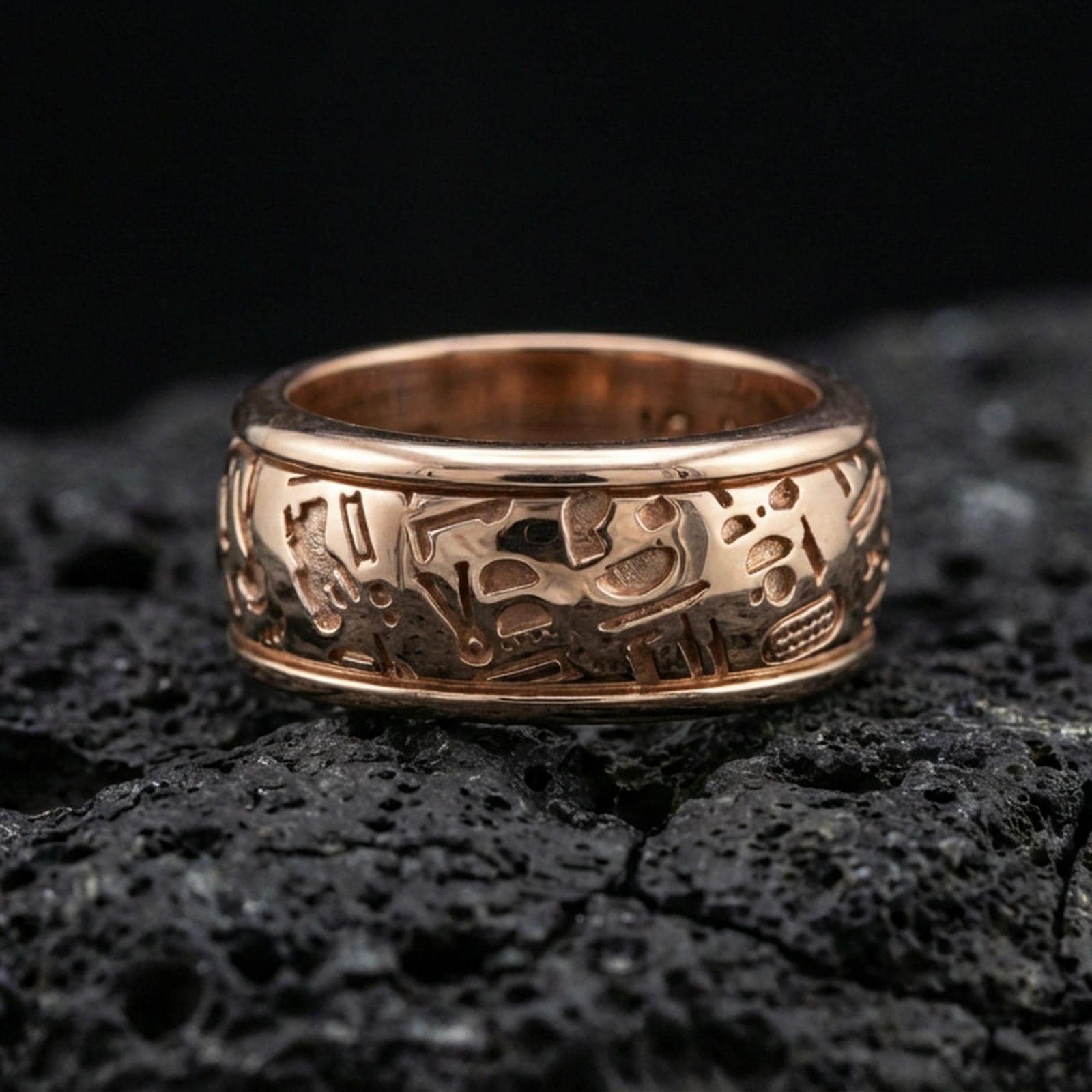 Rose gold plated hieroglyph band ring on volcanic stone, refined macro shot featuring soft rosy highlights and sharp hieroglyph engraving depth.