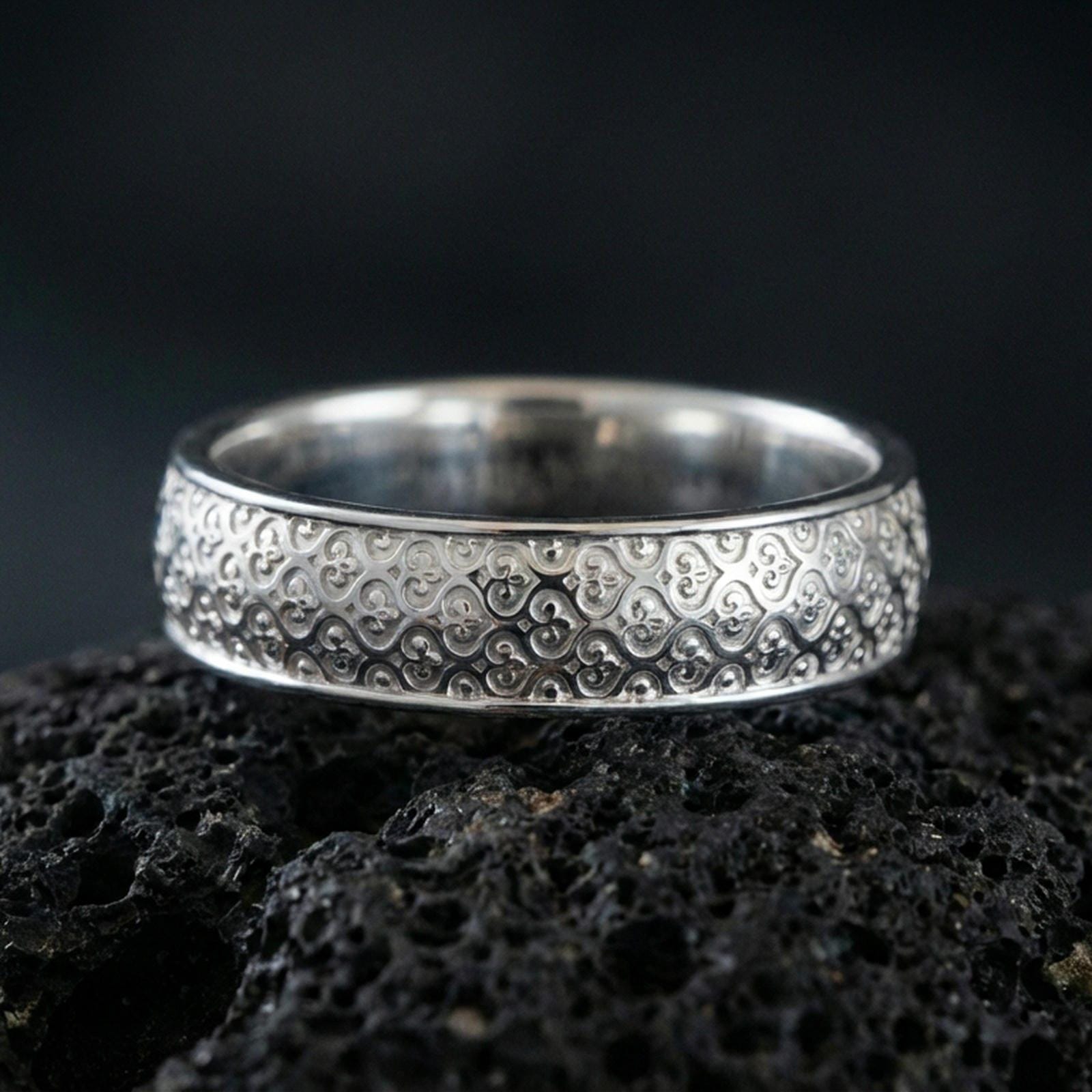 Polished silver fleur-de-lis band ring on volcanic stone, crisp product photo emphasizing the clean relief pattern and bright reflective edges.