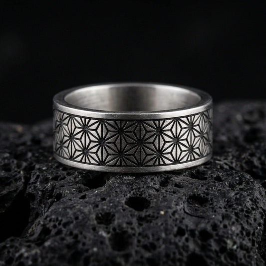 Oxidized sterling silver geometric floral band ring on volcanic stone, macro close-up highlighting the darkened engraved lattice pattern and crisp edges.