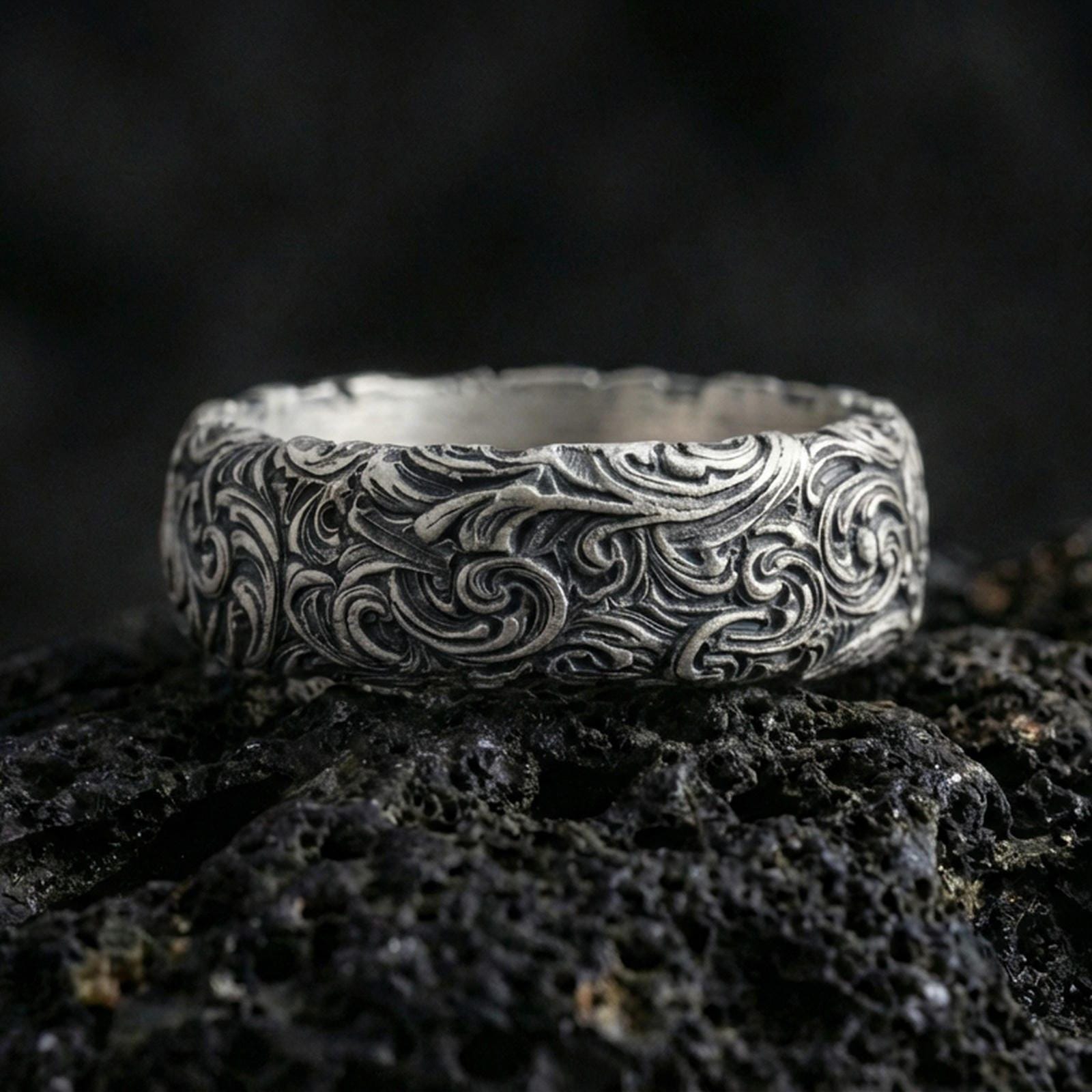 Oxidized sterling silver scrollwork band ring on volcanic stone, macro close-up highlighting deep engraved swirls and dark contrast.