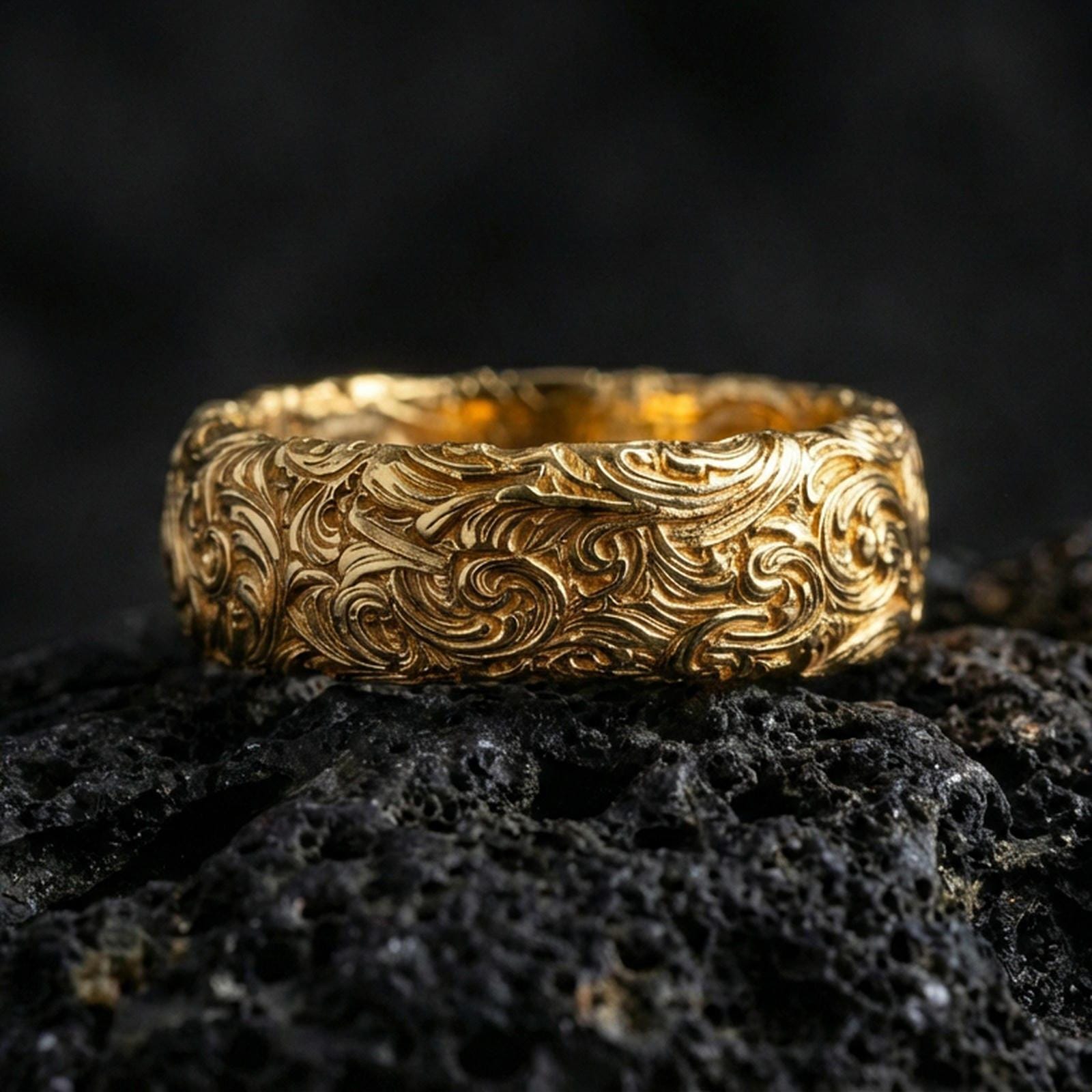 Gold plated scrollwork band ring on volcanic stone, premium macro shot showing warm gold tone across the detailed engraved filigree.