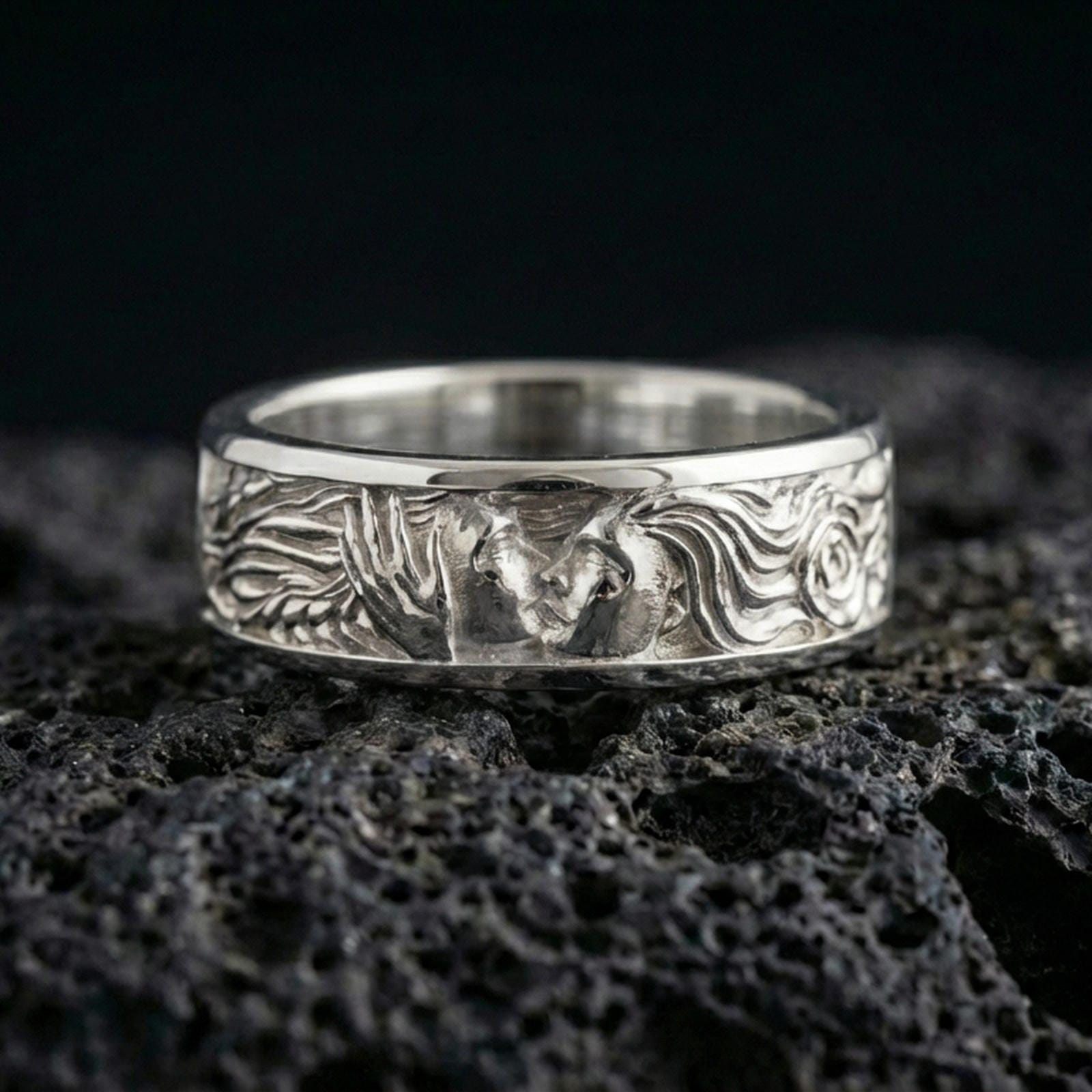 Polished silver lovers face ring on volcanic stone, clean product photo emphasizing bright shine and crisp relief details in the faces and hair.