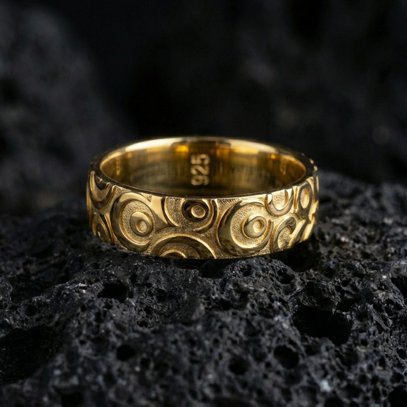 Gold plated geometric circle pattern ring on volcanic stone, premium macro photo showing warm gold tone across the repeating concentric design.