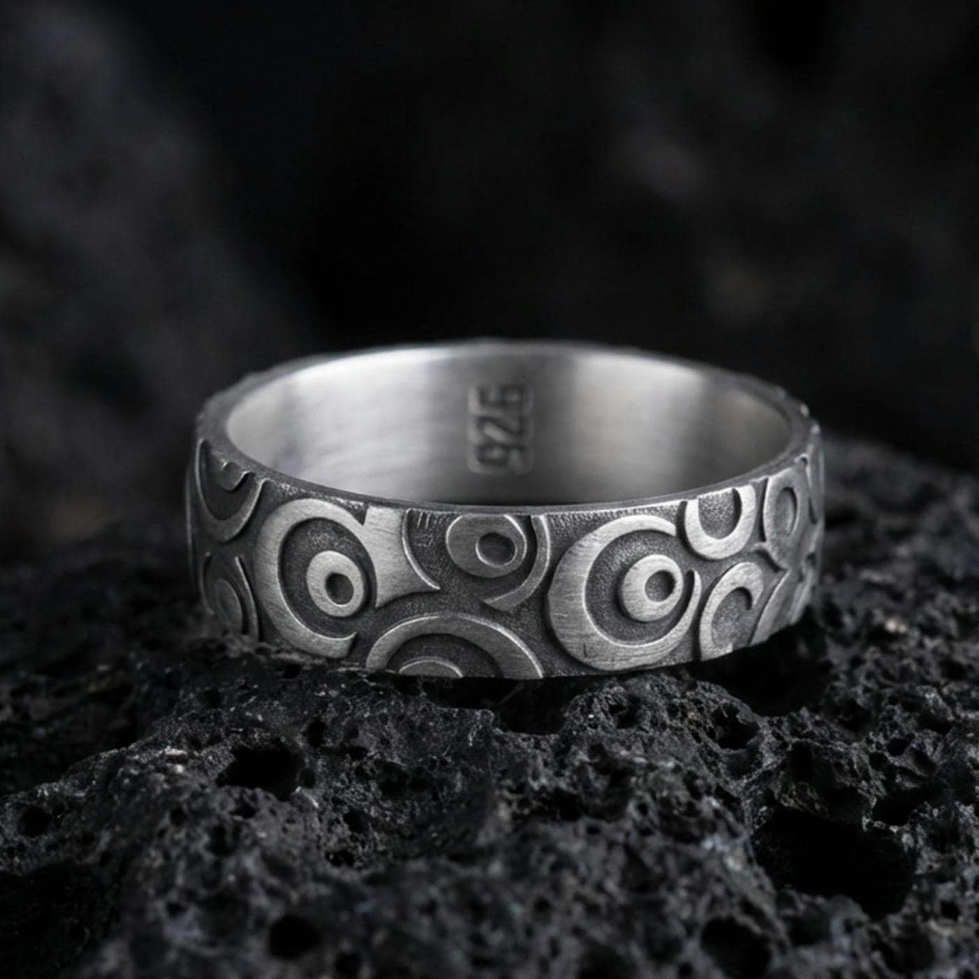 Oxidized sterling silver geometric circle pattern ring on volcanic stone, macro close-up highlighting the carved concentric motifs and dark antique contrast.