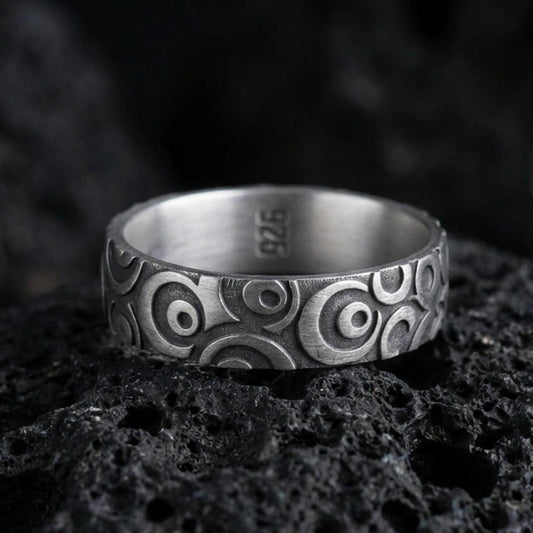Oxidized sterling silver geometric circle pattern ring on volcanic stone, macro close-up highlighting the carved concentric motifs and dark antique contrast.