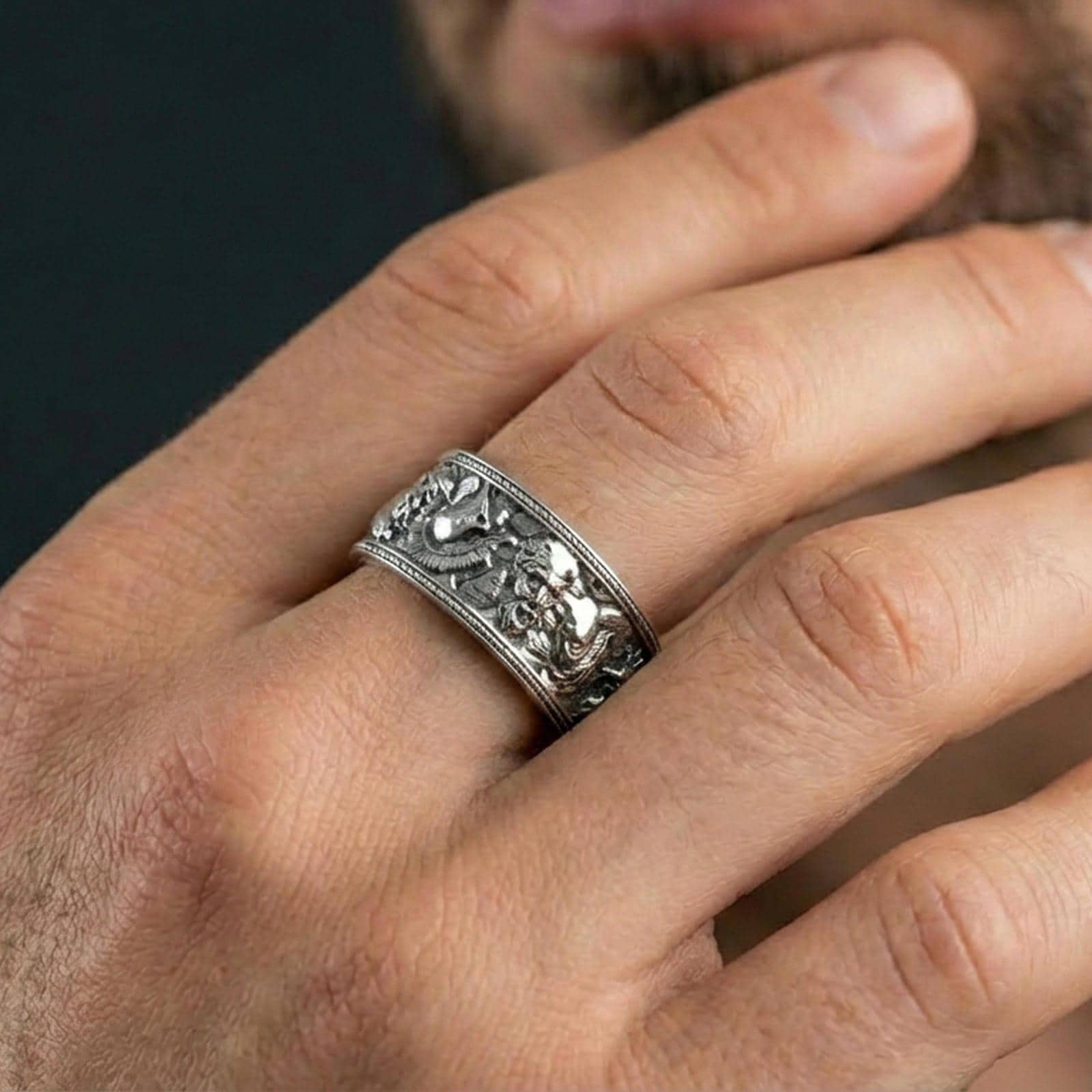 Polished silver mythic faces cuff band ring worn on a finger, lifestyle shot focusing on bright reflective finish and the detailed portrait band design.