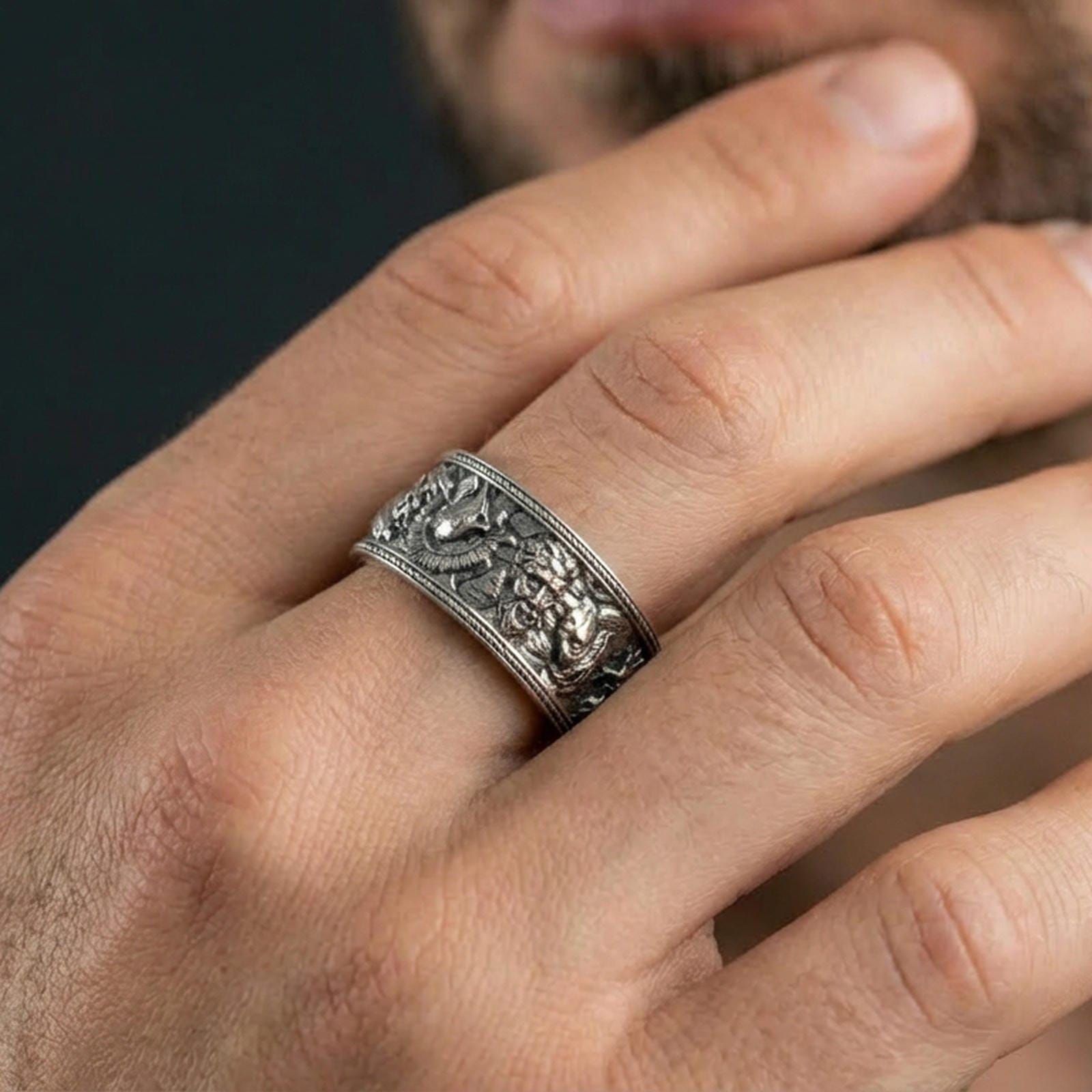 Oxidized sterling silver mythic faces cuff band ring worn on a finger, lifestyle wear image showing bold depth, shadowed recesses, and statement presence.
