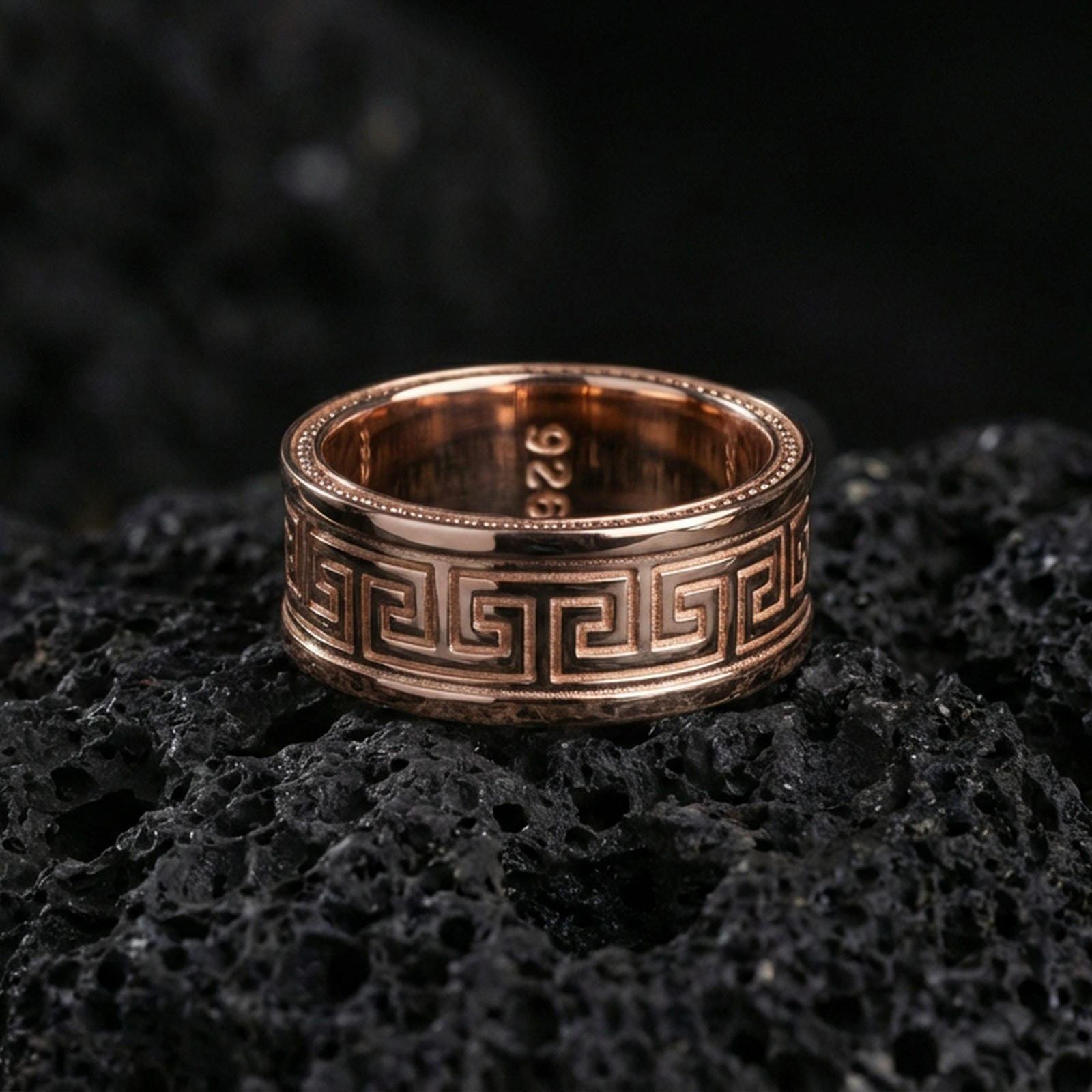 Rose gold plated Greek key spinner ring on volcanic stone, elegant macro shot capturing soft rose reflections on the Greek key band and brushed center texture.