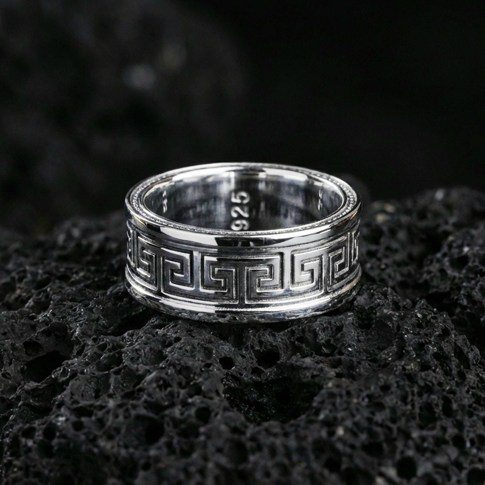 Polished silver Greek key spinner ring on volcanic stone, clean studio macro showing bright shine, sharp geometric pattern, and smooth comfort edges.