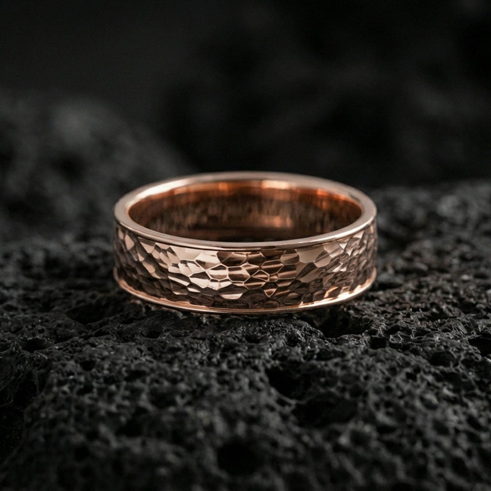 Rose gold plated hammered texture band ring on volcanic stone, elegant macro shot capturing soft rose reflections over the hammered detailing and rounded profile.