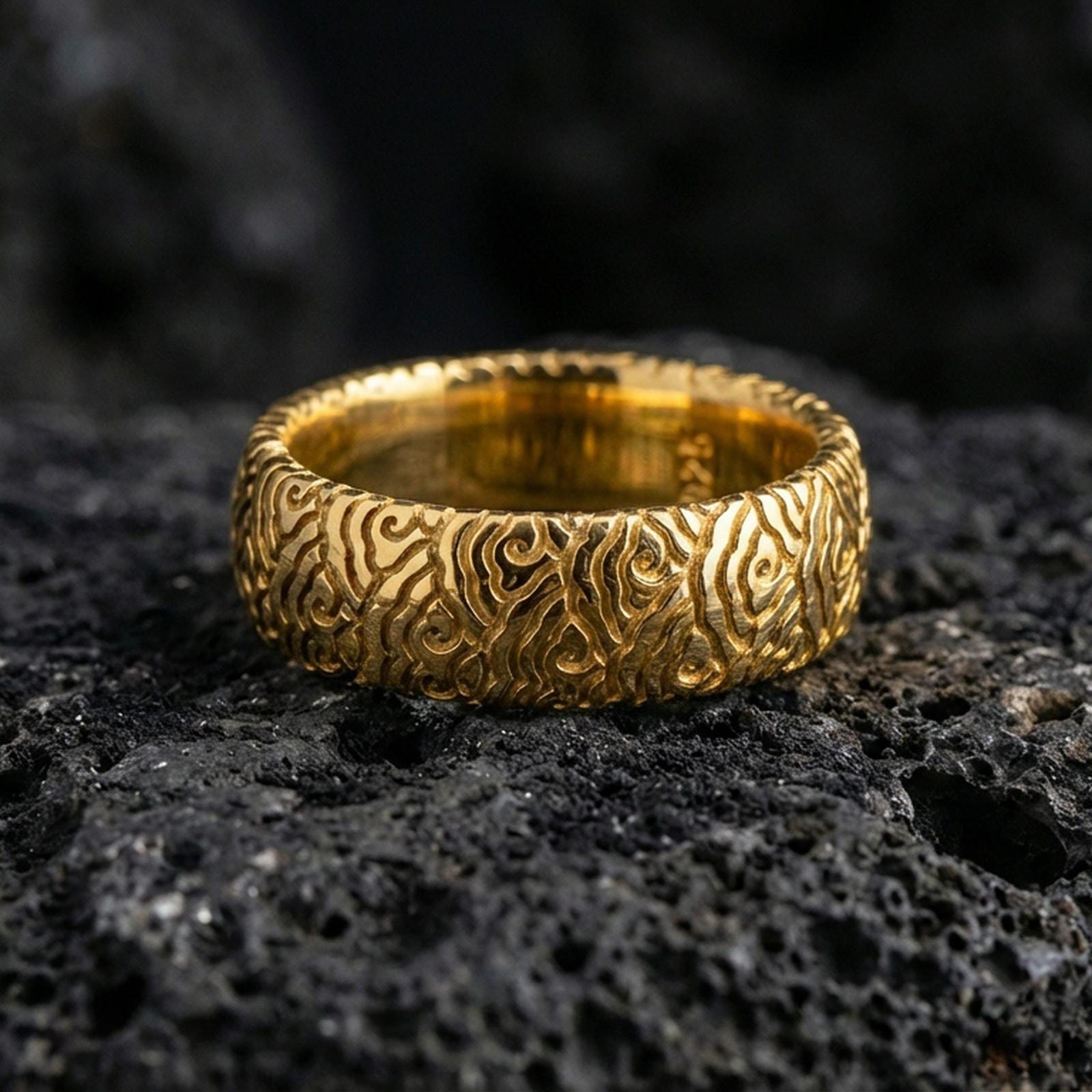 Gold plated wave pattern band ring on volcanic stone, premium macro shot showcasing warm gold tone across the flowing wave engraving and refined shine.