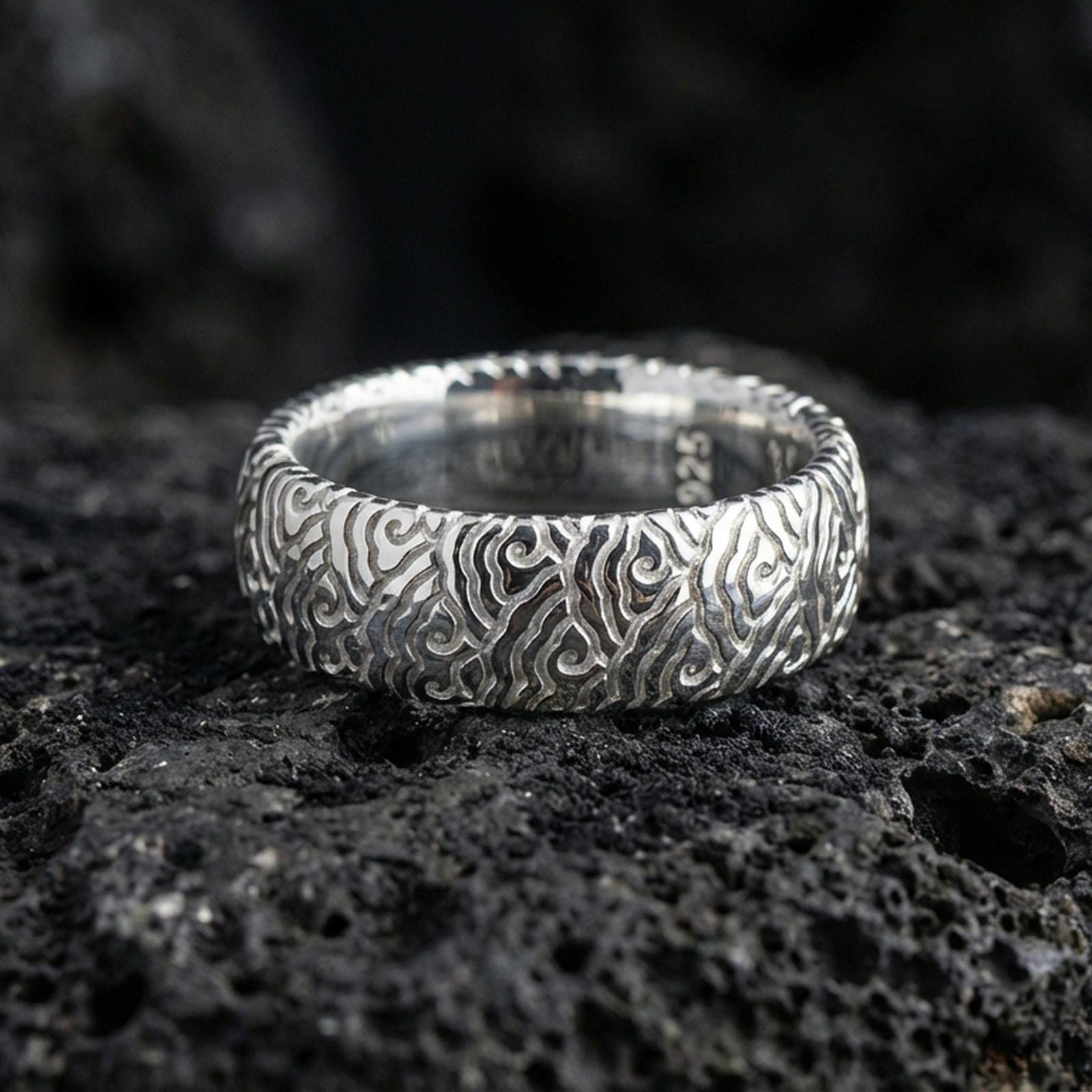 Polished silver wave pattern band ring on volcanic stone, clean studio macro emphasizing crisp engraved lines, bright reflections, and smooth comfort edges.