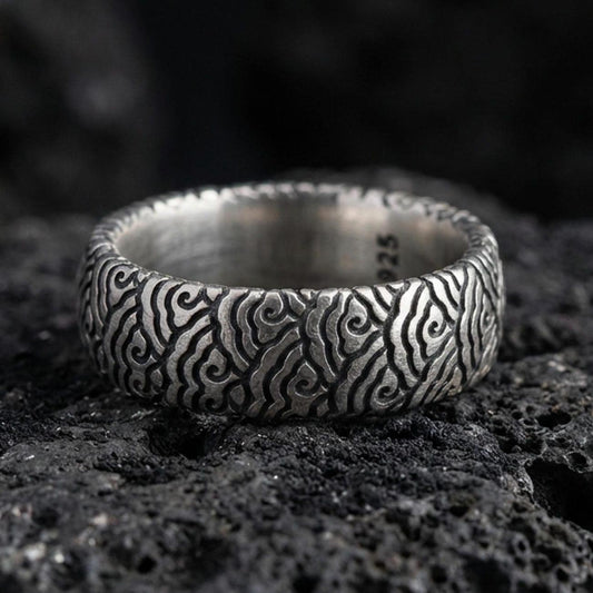 Oxidized sterling silver wave pattern band ring on volcanic stone, macro close-up highlighting deepened grooves, textured contrast, and vintage character.