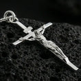 Load image into Gallery viewer, Polished silver crucifix pendant on volcanic stone, clean macro shot emphasizing sharp detailing on the figure, crisp edges, and bright reflective finish.

