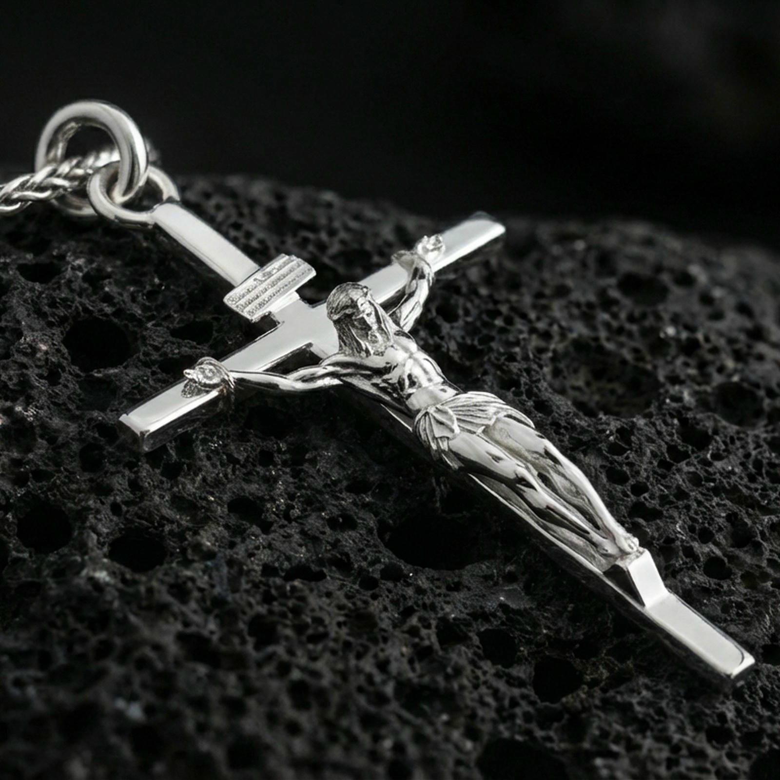 Polished silver crucifix pendant on volcanic stone, clean macro shot emphasizing sharp detailing on the figure, crisp edges, and bright reflective finish.