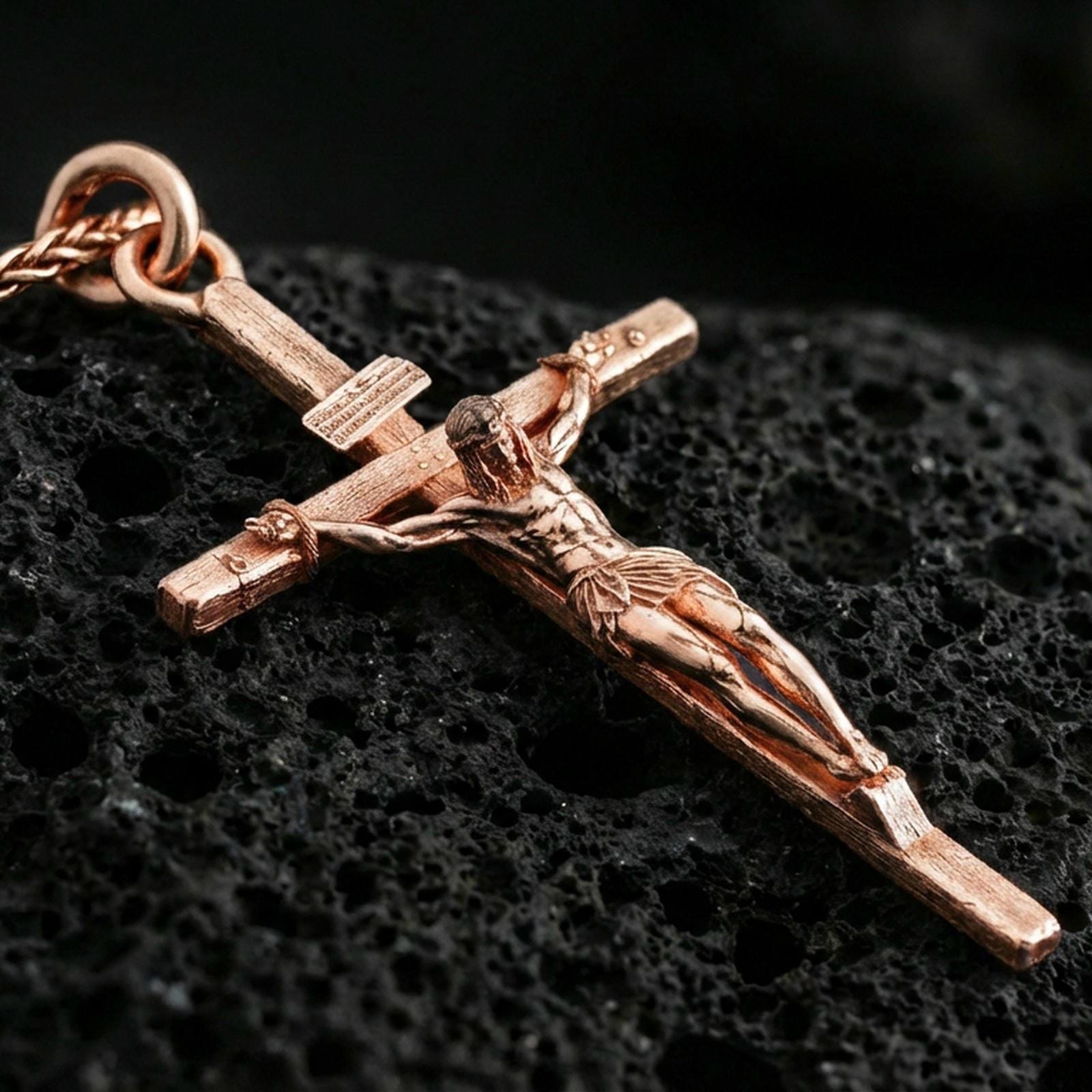 Rose gold plated crucifix pendant on volcanic stone, elegant macro shot capturing soft rose reflections, refined contours, and high-relief craftsmanship.