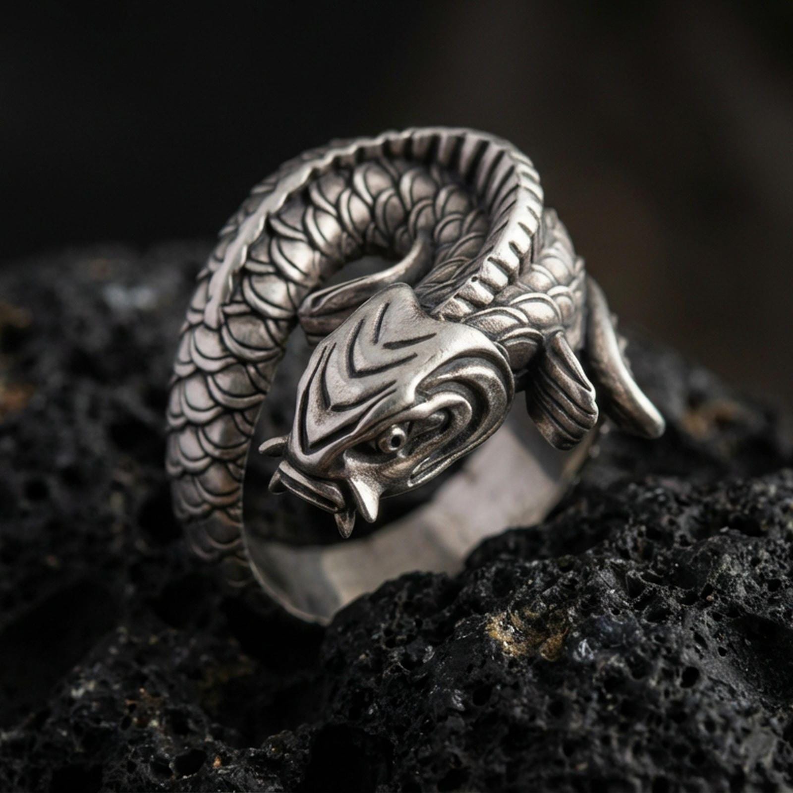 Oxidized sterling silver koi fish wrap ring on volcanic stone, macro close-up highlighting the coiled body, deep scale texture, and antique contrast shadows.