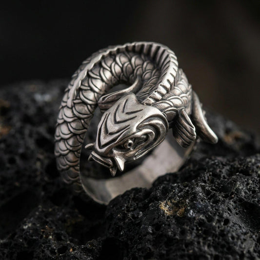 Oxidized sterling silver koi fish wrap ring on volcanic stone, macro close-up highlighting the coiled body, deep scale texture, and antique contrast shadows.