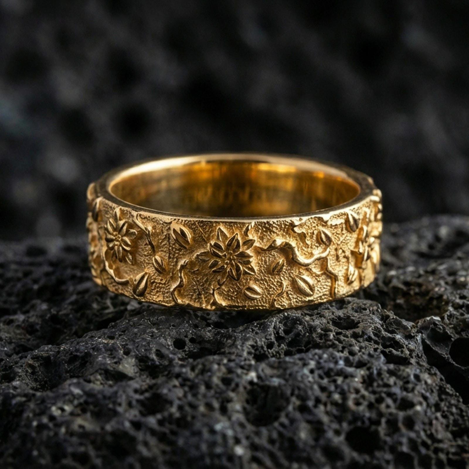 Gold plated floral engraved band ring on volcanic stone, premium macro close-up showcasing warm gold tone across the floral pattern and textured background.