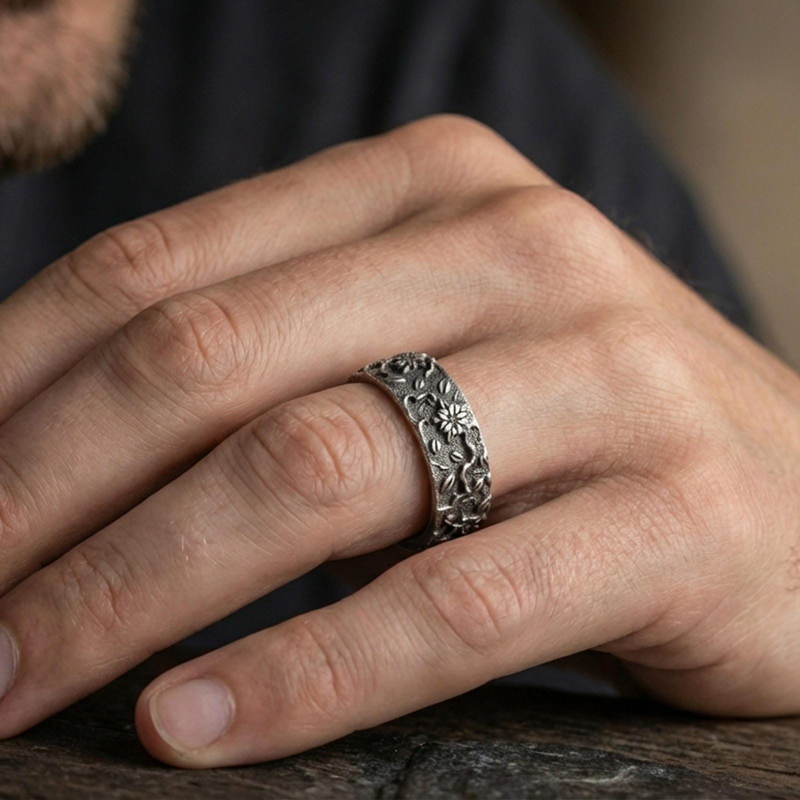 Oxidized sterling silver floral engraved band ring worn on the finger, lifestyle photo focusing on bold antique contrast and detailed botanical relief.