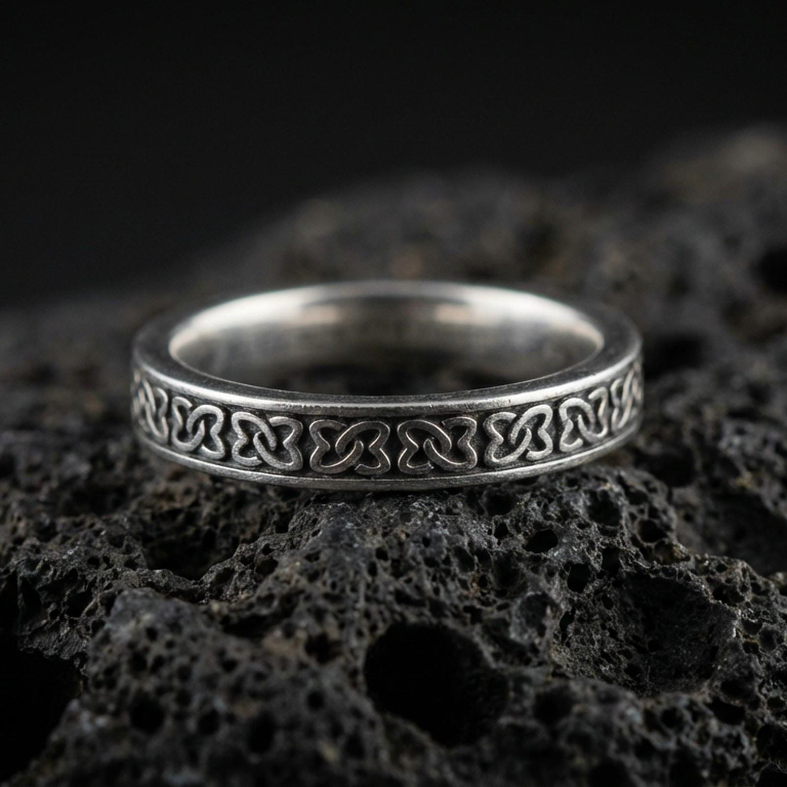 Oxidized sterling silver Celtic knot band ring on volcanic stone, macro close-up highlighting the repeating interlaced pattern and antique contrast.