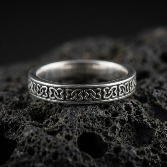Oxidized sterling silver Celtic knot band ring on volcanic stone, macro close-up highlighting the repeating interlaced pattern and antique contrast.
