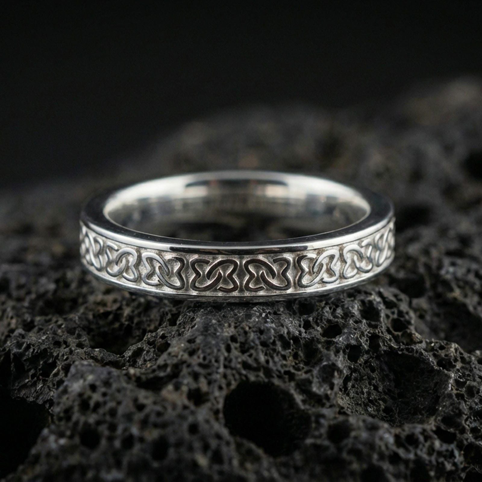 Polished silver Celtic knot band ring on volcanic stone, crisp macro shot emphasizing clean shine, smooth edges, and detailed knotwork.