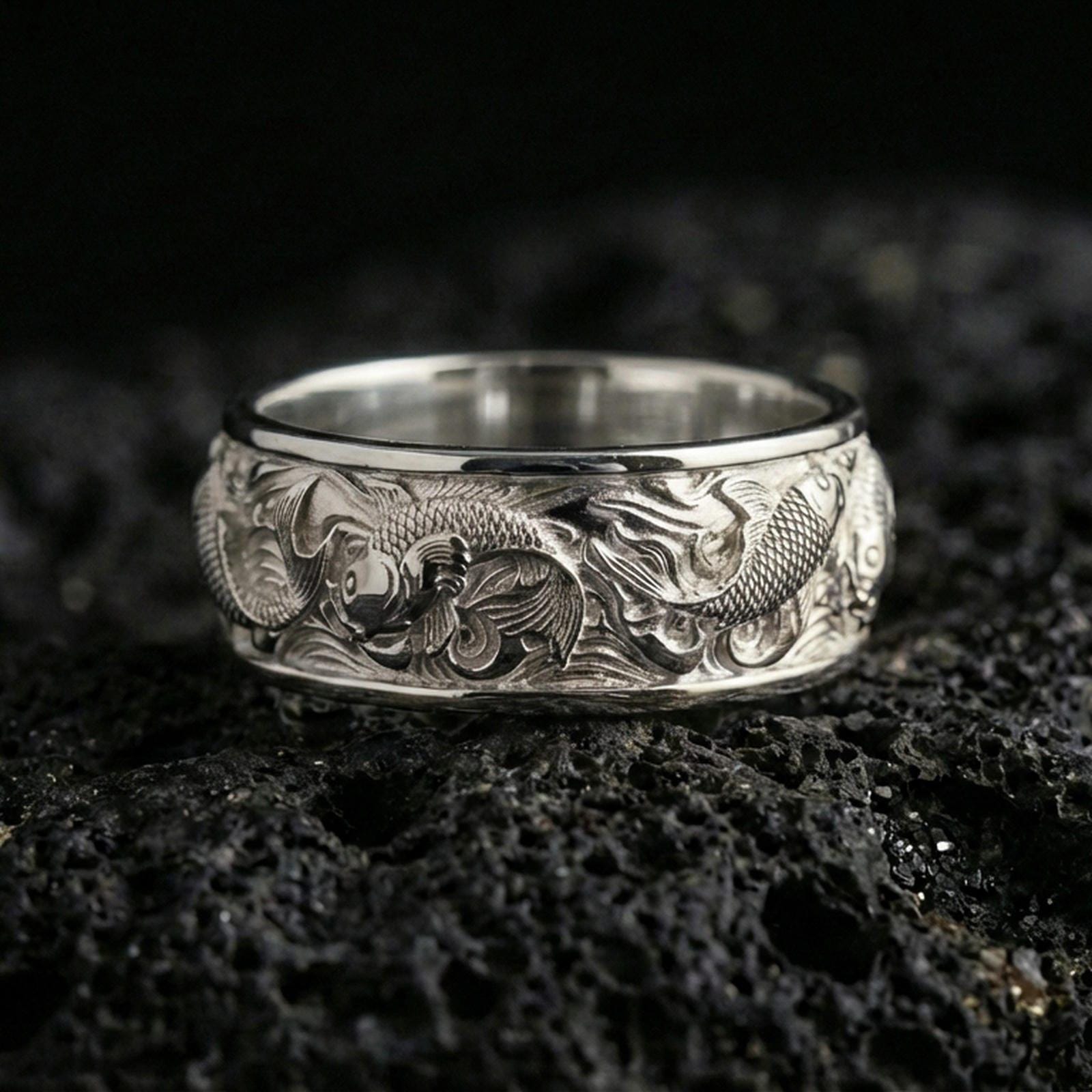 Polished silver koi fish band ring on volcanic stone, crisp macro shot highlighting smooth edges, bright shine, and detailed koi scale texture.