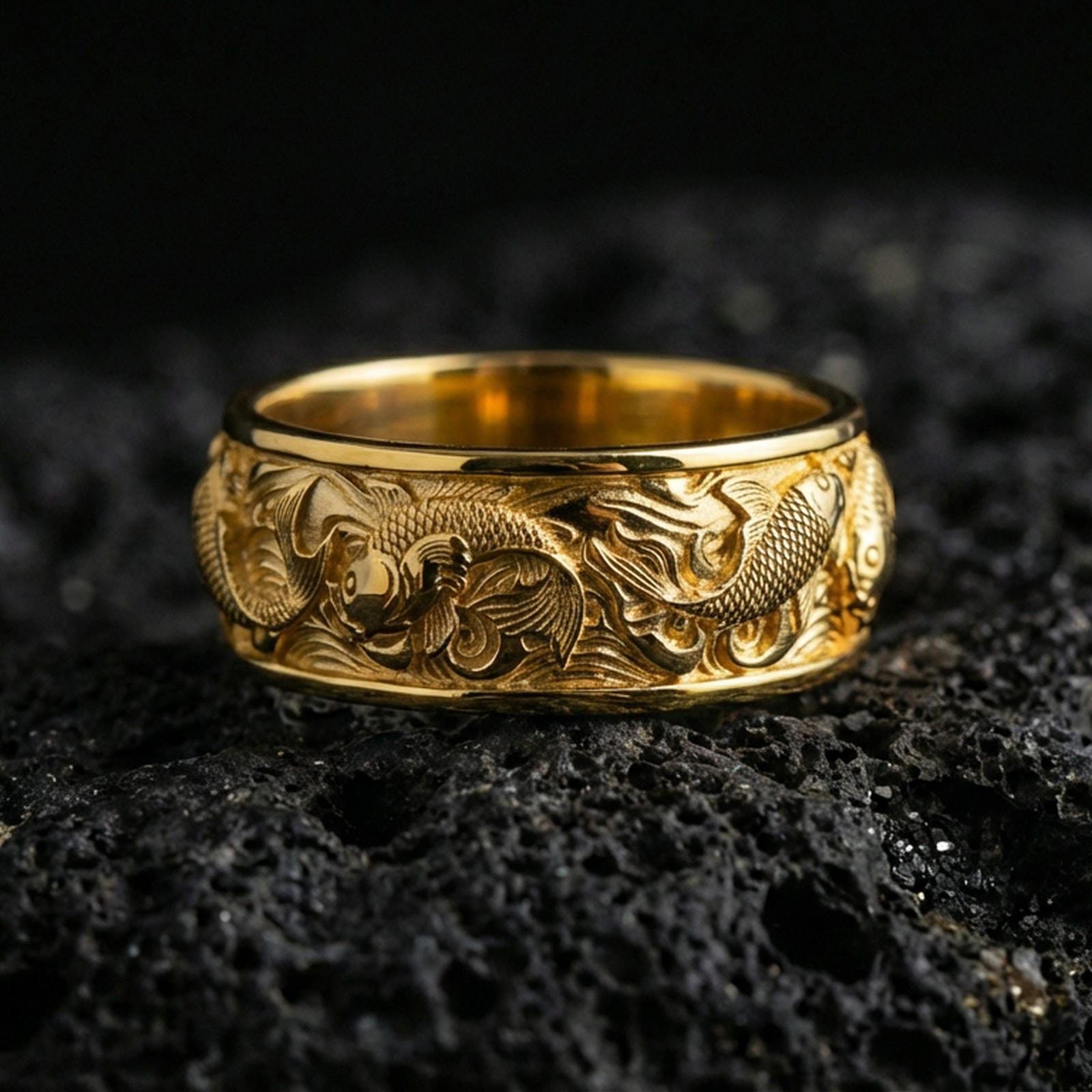 Gold plated koi fish band ring on volcanic stone, premium macro photo showcasing warm gold tone over the koi motifs and flowing water pattern.