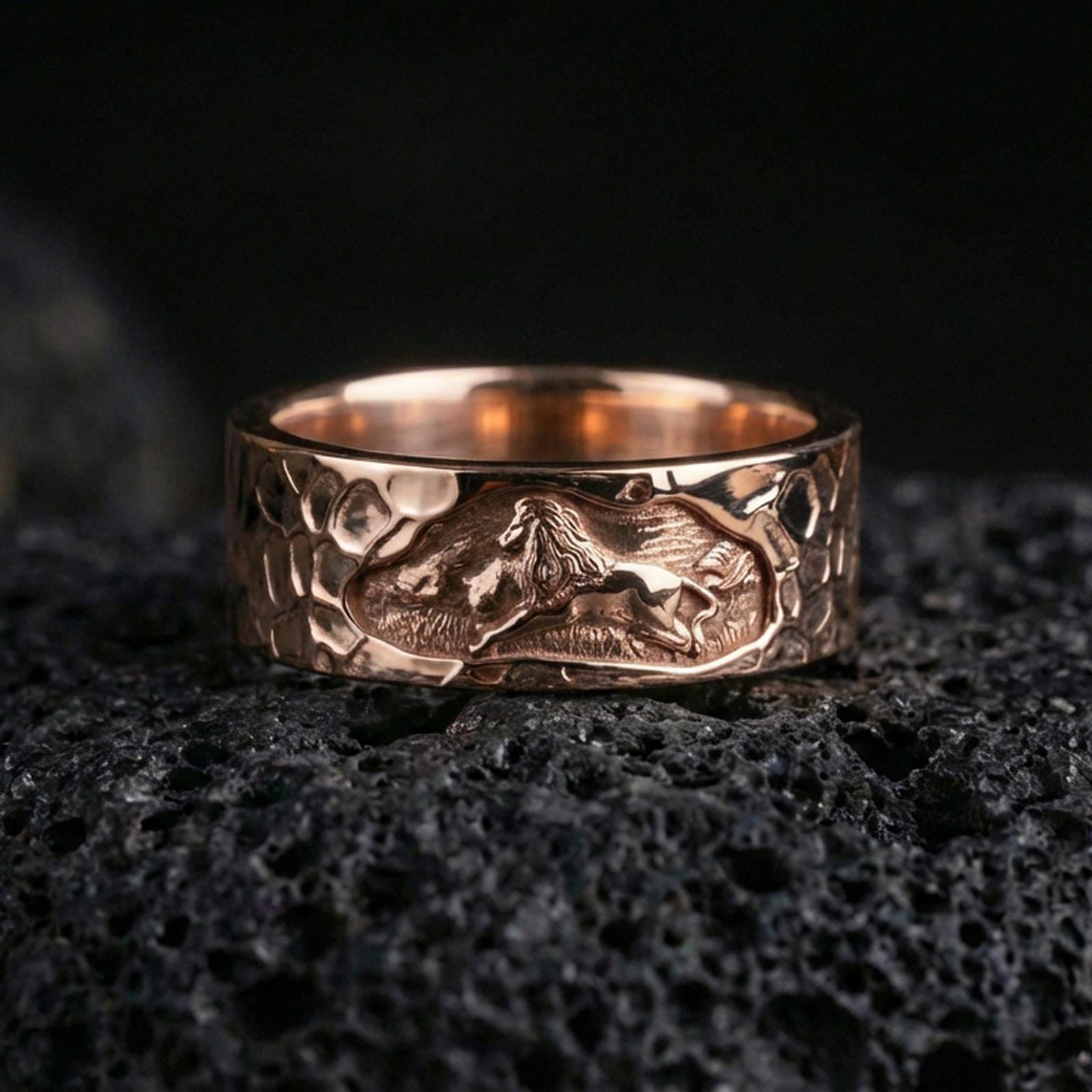 Rose gold plated lion band ring on volcanic stone, refined macro close-up capturing soft rose reflections across the lion relief and hammered surface.
