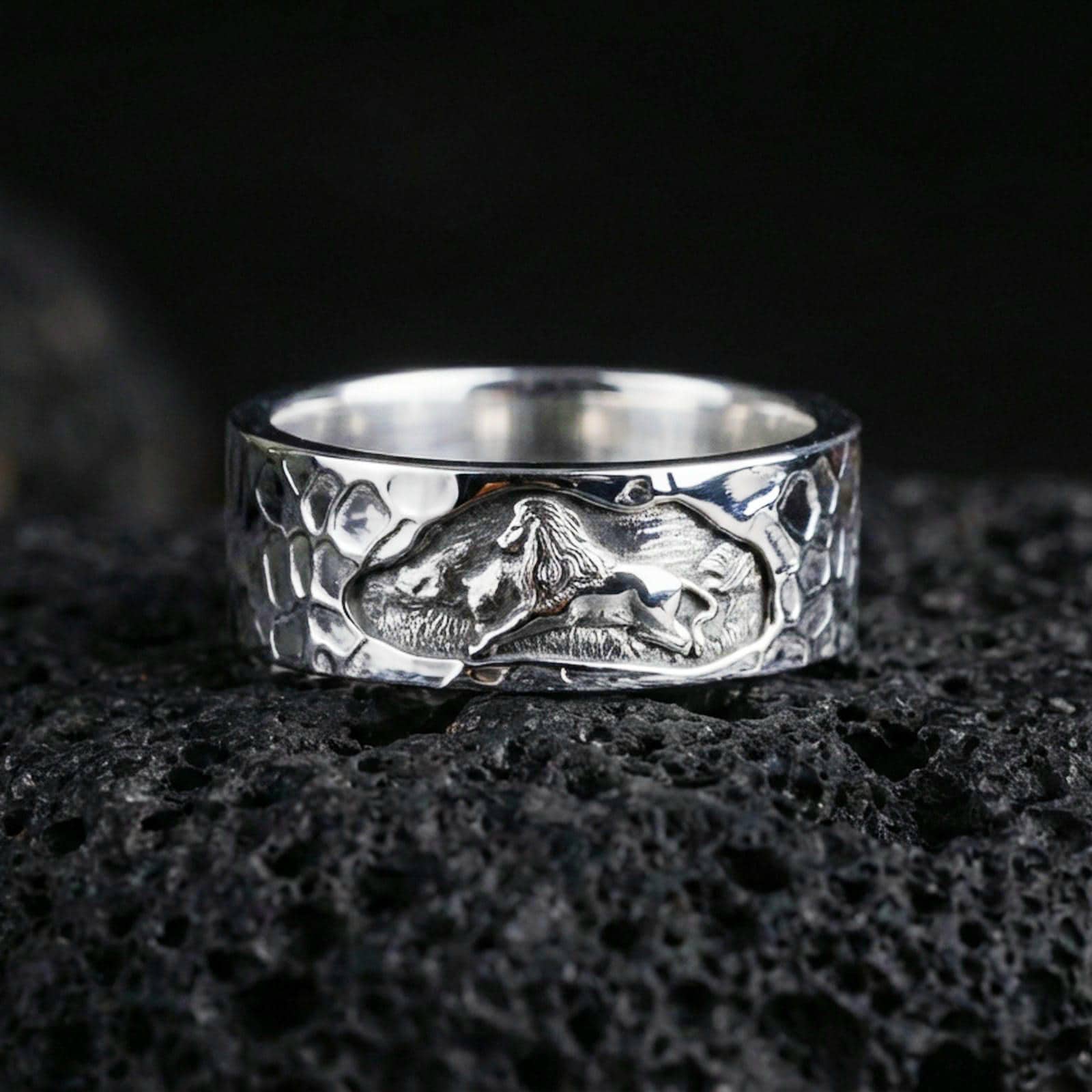 Polished silver lion band ring on volcanic stone, crisp macro shot emphasizing bright edges, smooth interior, and high-definition lion engraving.