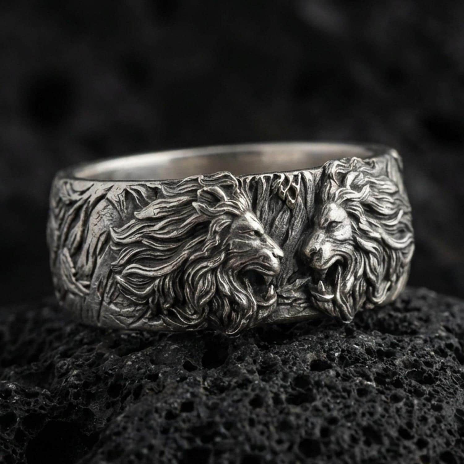 Oxidized sterling silver lion head ring on volcanic stone, macro close-up highlighting deep shadow contrast, roaring lion relief, and sculpted mane texture.