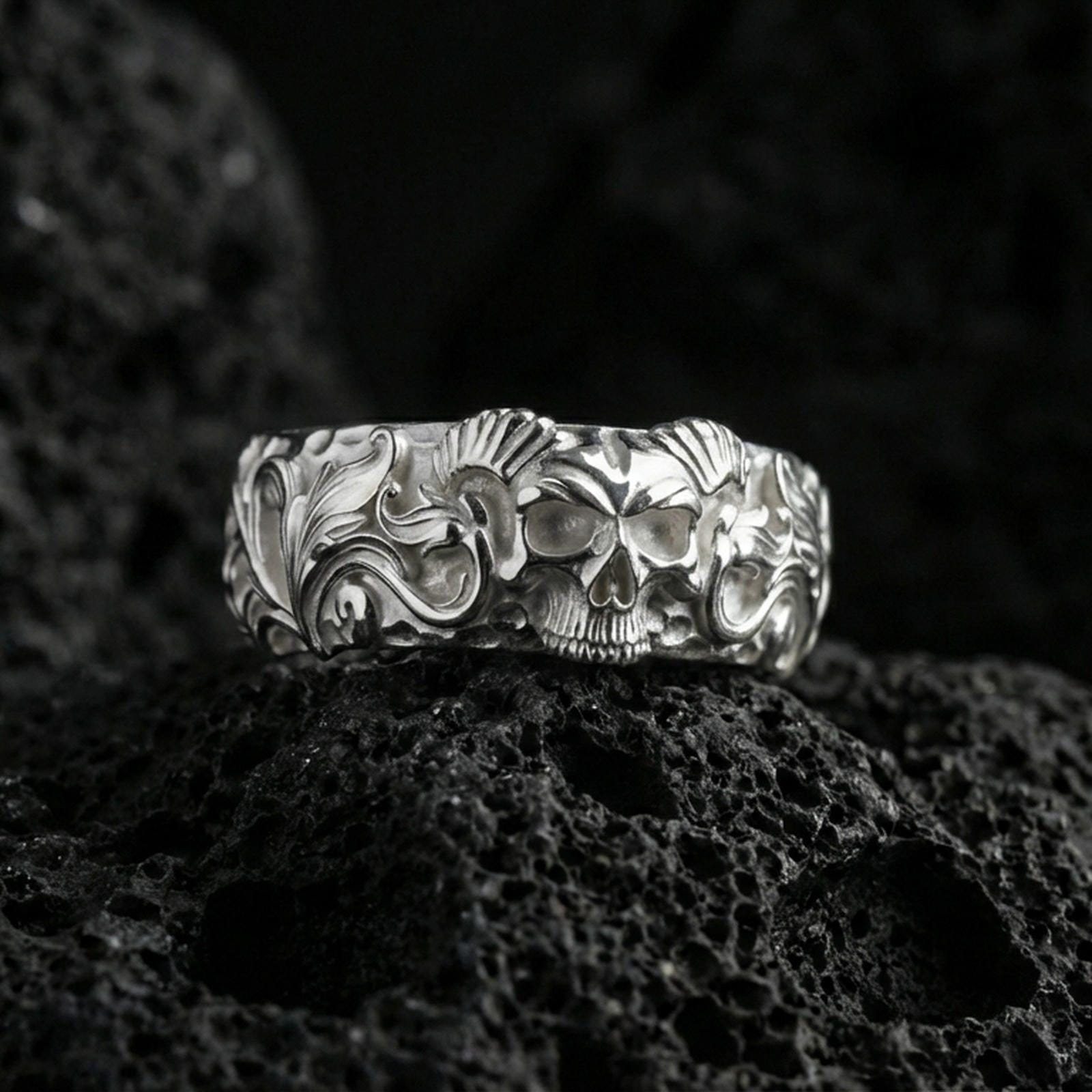 Polished silver skull ring on volcanic stone, sharp macro photo emphasizing clean shine, crisp skull contours, and high-relief detailing.