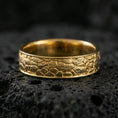 Load image into Gallery viewer, Gold plated pebble texture band ring on volcanic stone, premium macro shot capturing warm gold tone across the hammered pebble pattern and clean silhouette.
