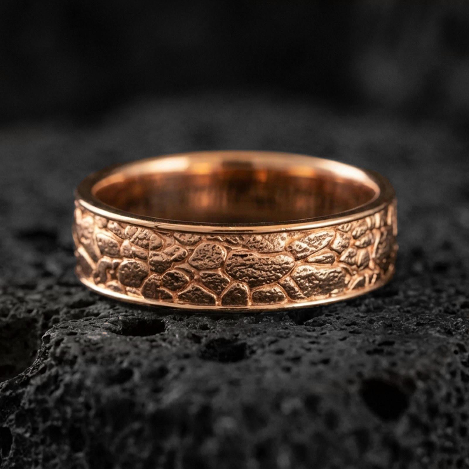 Rose gold plated pebble texture band ring on volcanic stone, refined macro close-up showcasing soft rose sheen with the rugged pebble texture and smooth comfort edges.