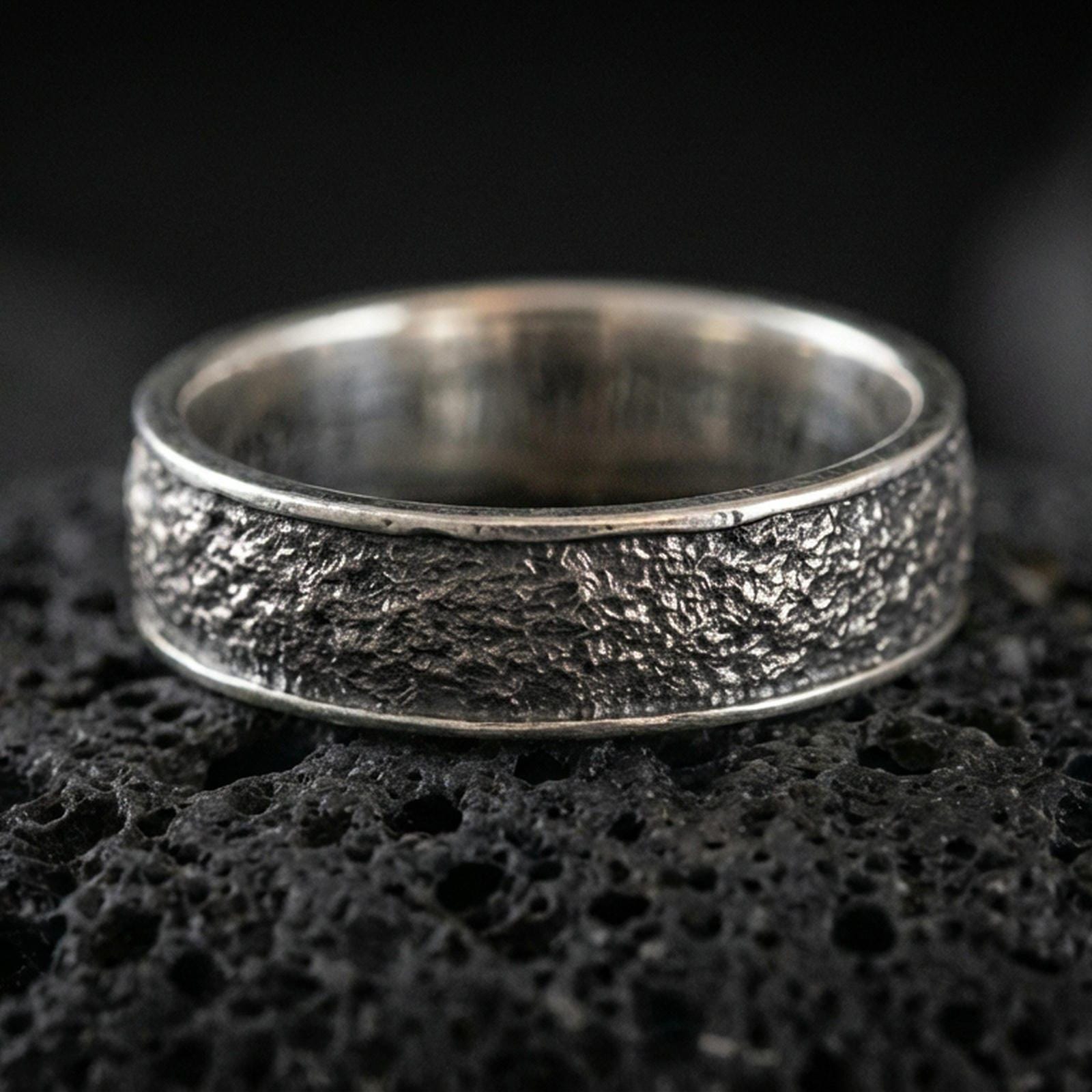 Oxidized sterling silver bark texture band ring on volcanic stone, macro close-up highlighting rugged tree-bark relief and deep shadowed contrast.