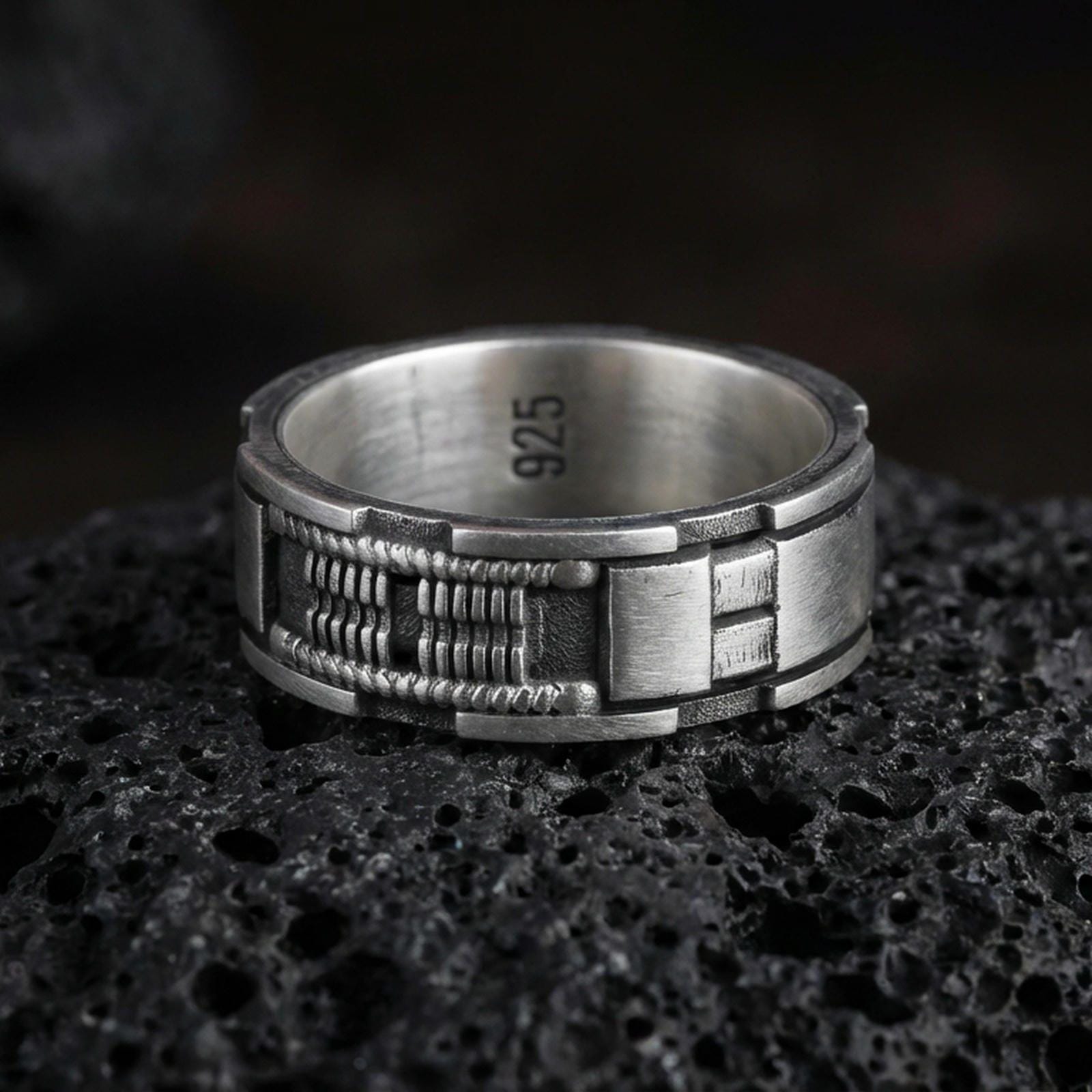 Oxidized sterling silver sci-fi band ring on volcanic stone, macro close-up highlighting the industrial panel texture, recessed details, and darkened contrast.