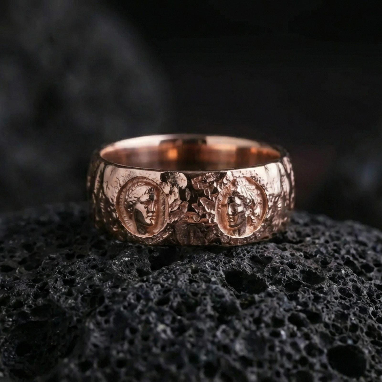 Rose gold plated Greek sculpture ring on volcanic stone, refined macro close-up showing soft rose warmth, detailed cameo faces, and luxury finish depth.