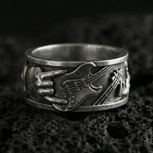 Oxidized sterling silver guitar ring on volcanic stone, macro close-up highlighting the raised electric guitar and hand detail with deep vintage patina.
