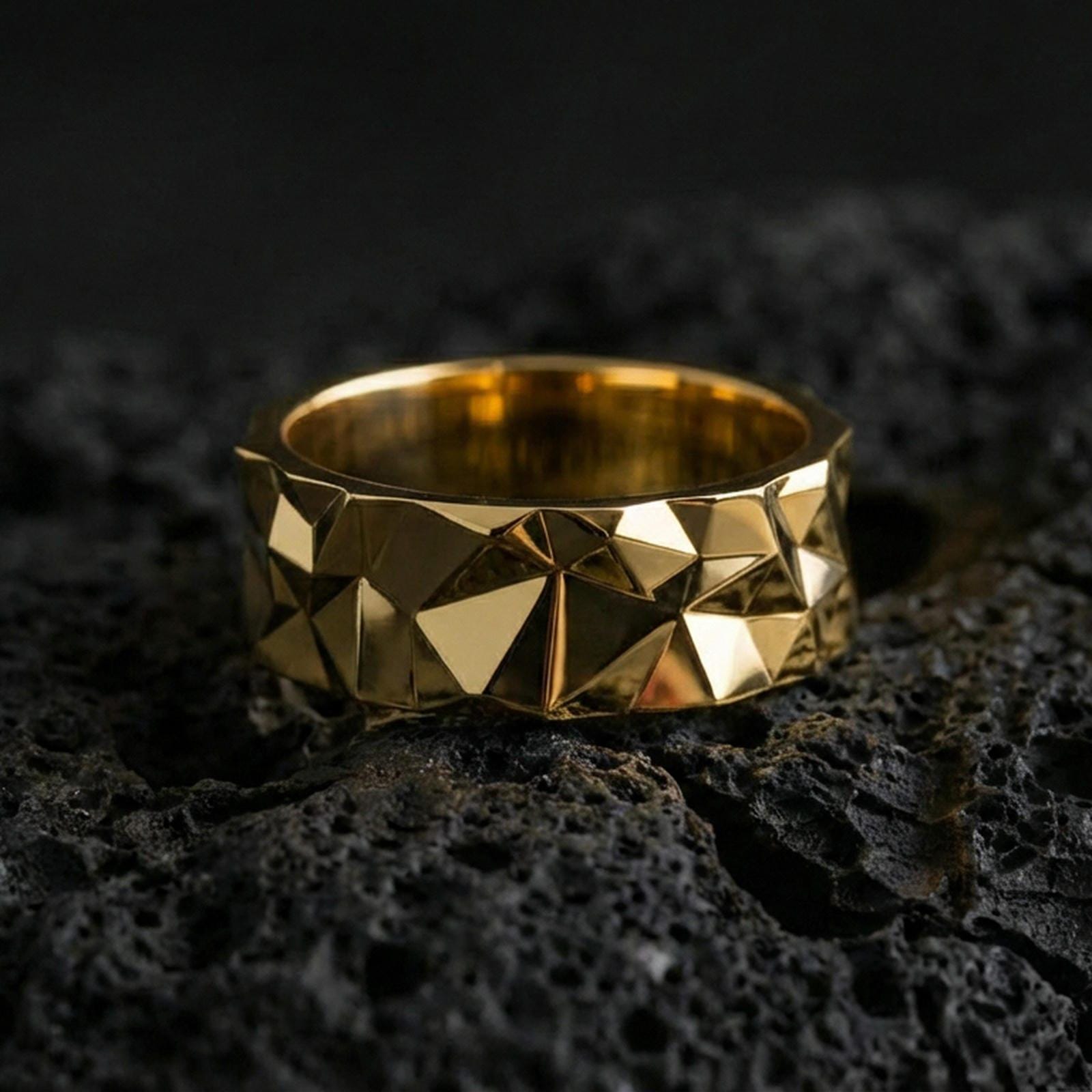 Gold plated faceted geometric band ring on volcanic stone, luxury macro photo showcasing warm gold tone across the pyramid facets and sculpted edges.