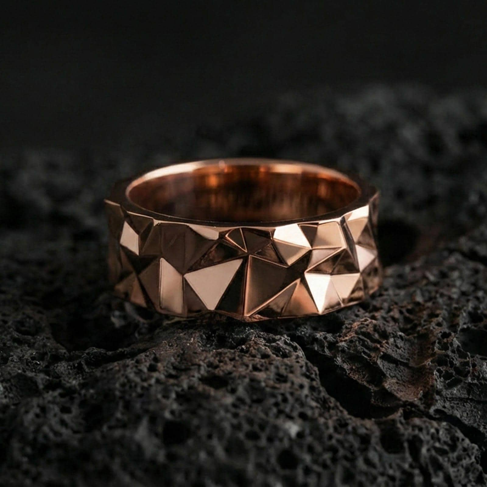 Rose gold plated faceted geometric band ring on volcanic stone, refined macro close-up capturing soft rose warmth, sharp geometry, and premium dimensional highlights.