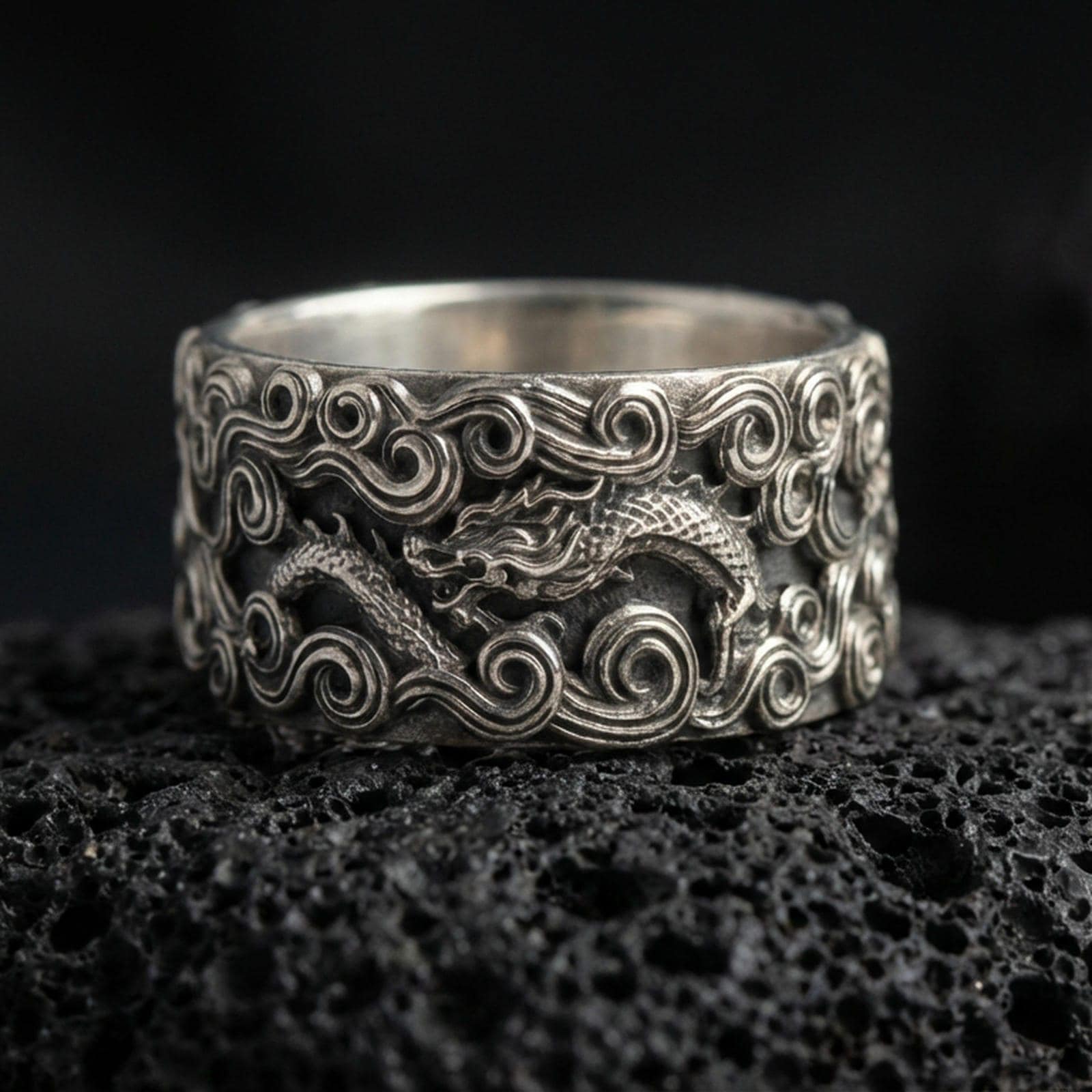 Oxidized sterling silver dragon cloud band ring on volcanic stone, macro close-up highlighting raised swirling clouds and detailed dragon scales.
