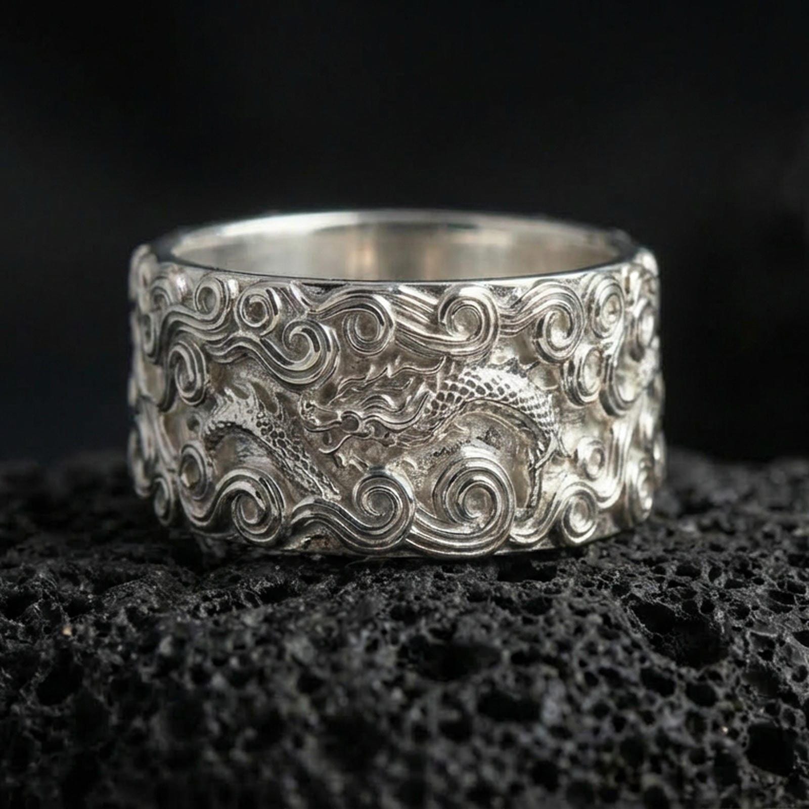 Polished silver dragon cloud band ring on volcanic stone, sharp macro photo emphasizing bright reflections, crisp relief, and layered wave scrollwork.