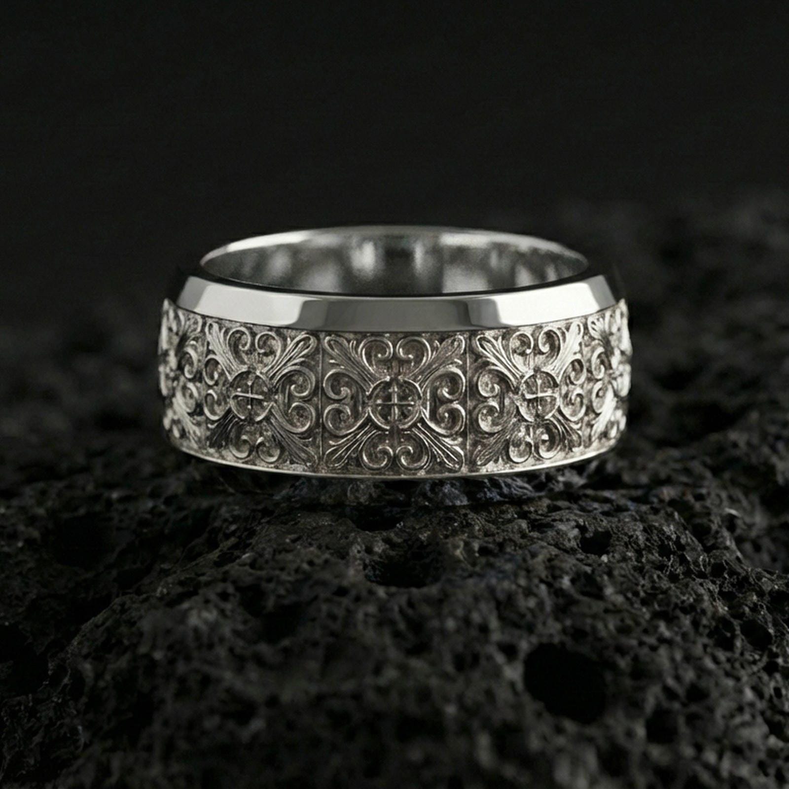 Polished silver cross scrollwork band ring on volcanic stone, crisp macro photo highlighting bright shine, clean edges, and symmetrical baroque engraving.