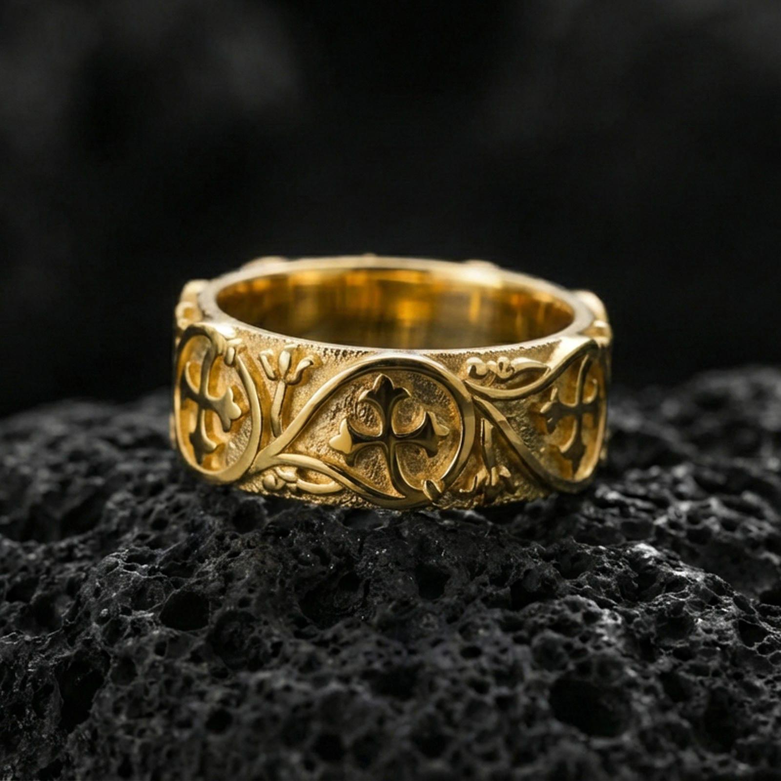 Gold plated quatrefoil cross band ring on volcanic stone, luxury macro shot capturing warm gold tone across the central cross emblems and flowing filigree lines.