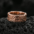 Load image into Gallery viewer, Rose gold plated quatrefoil cross band ring on volcanic stone, refined macro close-up emphasizing soft rose warmth, rounded band profile, and ornate cross motifs.
